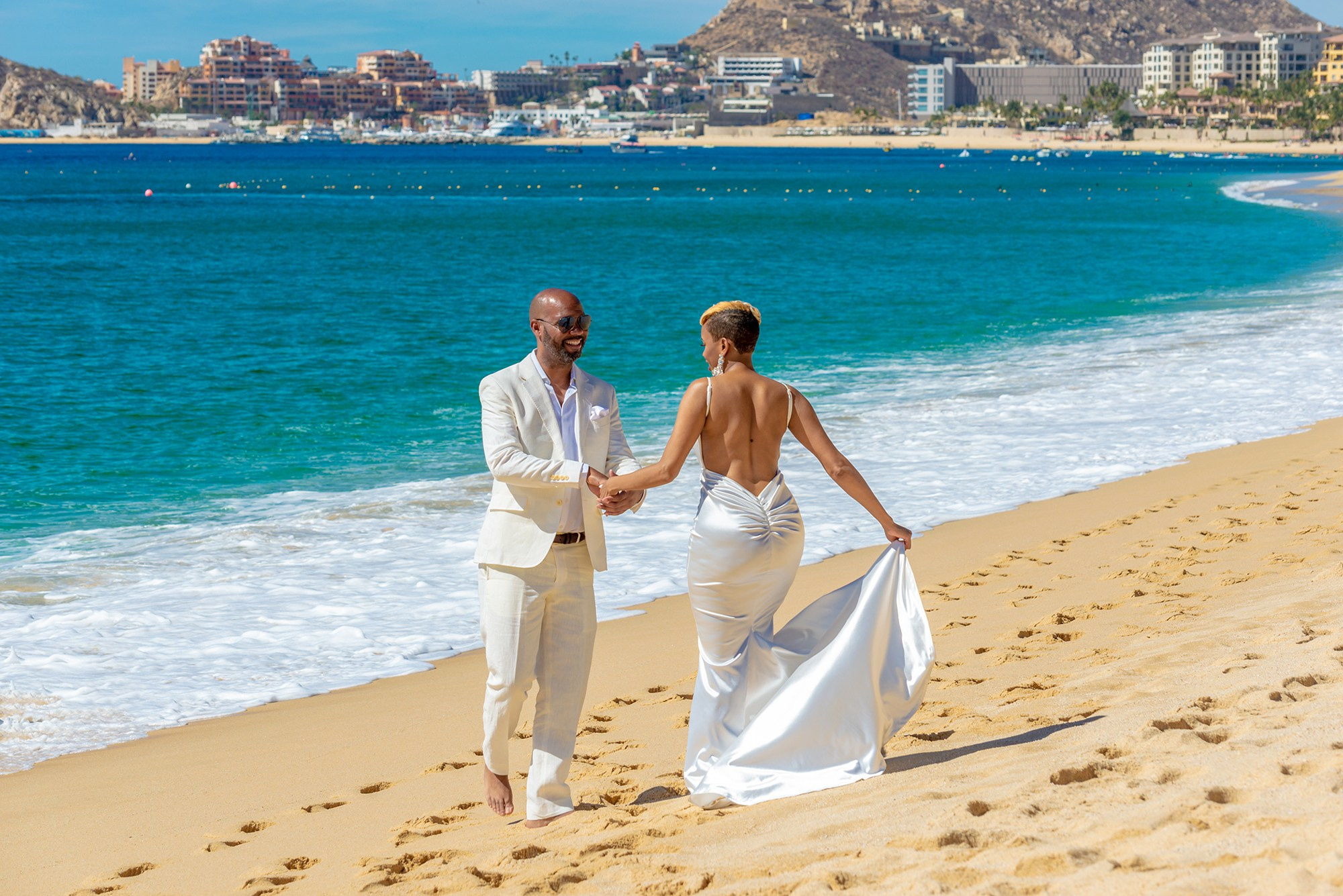 Smiling bride and groom candid portrait on Medano Beach with hotel zone in Los Cabos