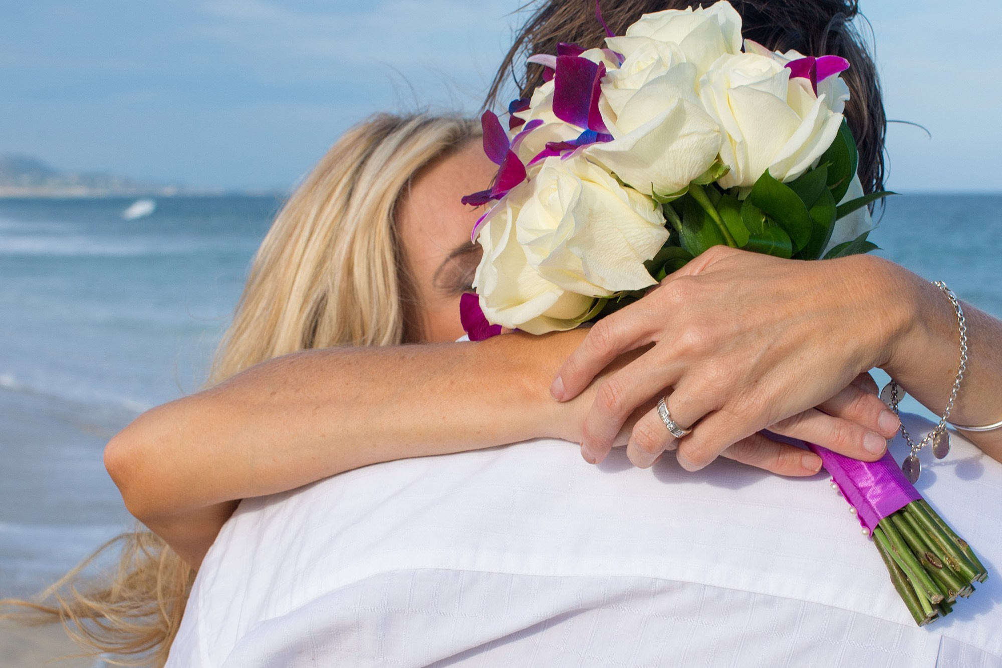 Bride embracing groom with bouquet and ring detail during beach wedding in Los Cabos