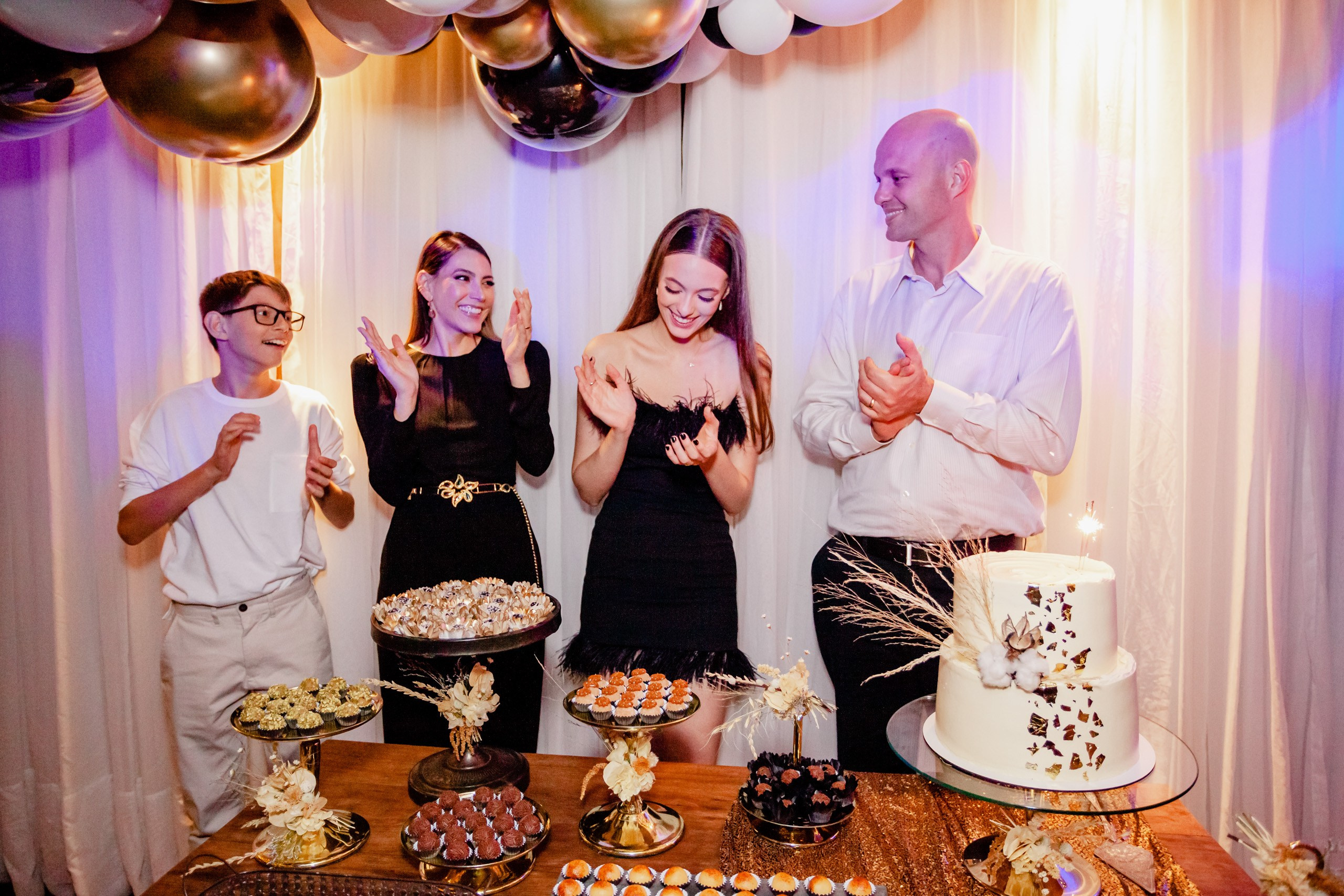 Fotógrafo festa de aniversário em Itajaí; momento alegre em que a aniversariante e a família batem palmas ao redor da mesa decorada com bolo e doces.