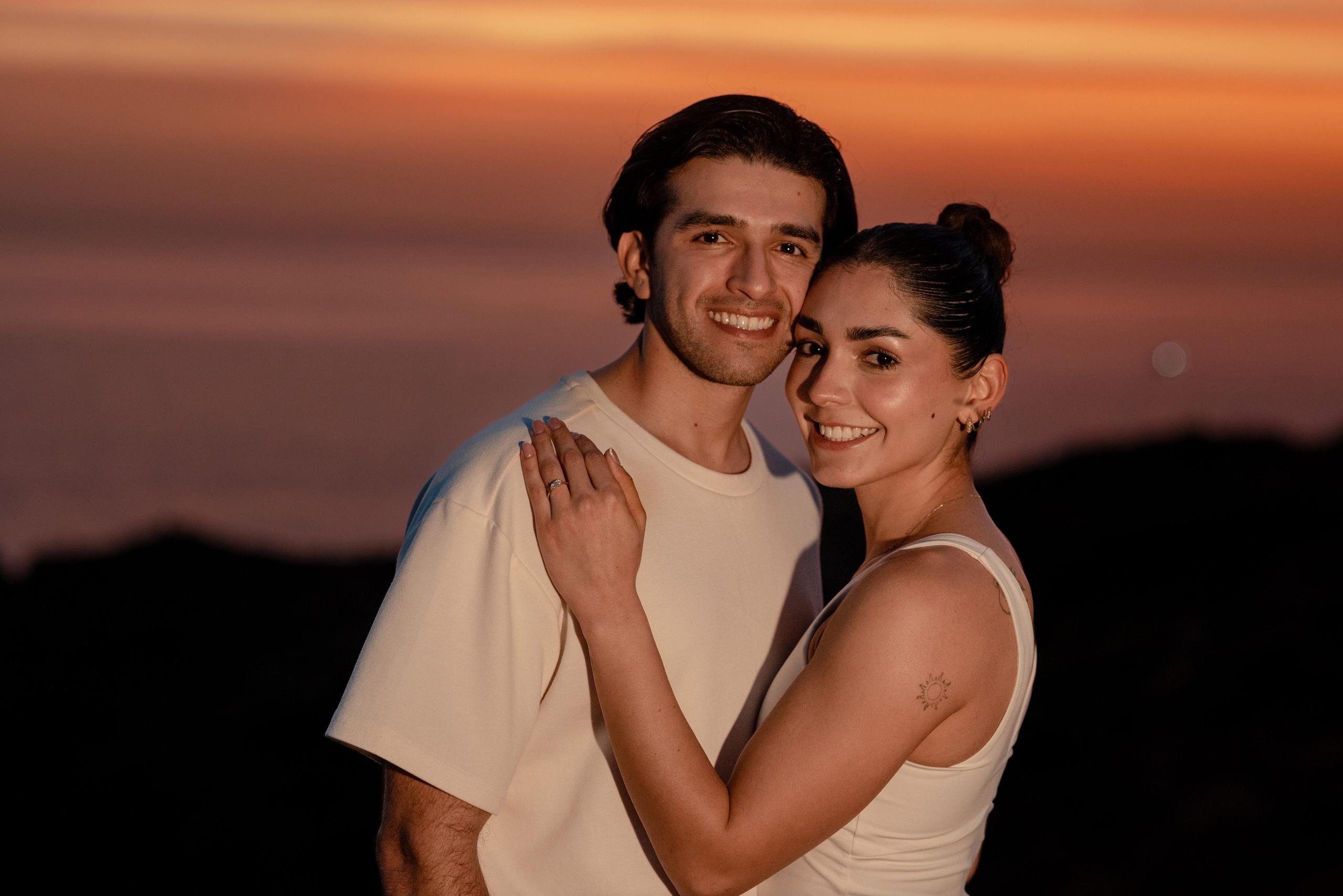 Couple embracing with panoramic view of Punta Lobos bay and cliffs during engagement session, Todos Santos Mexico