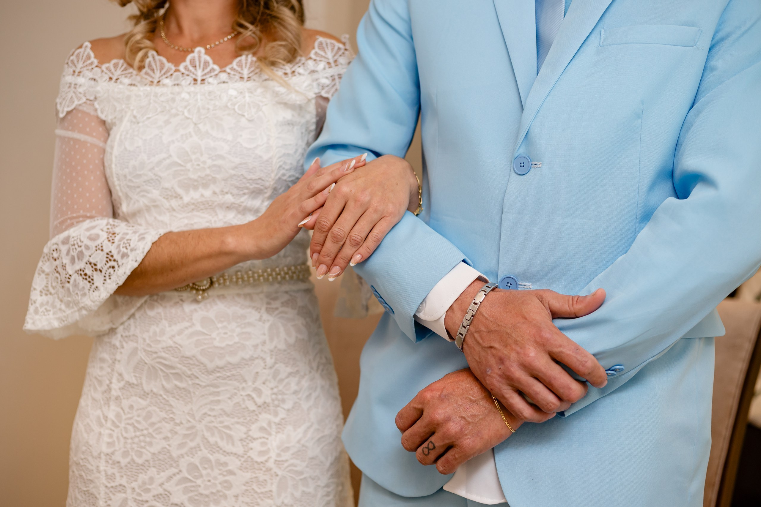 Fotógrafo de casamento civil em Navegantes; close detalhado das mãos da noiva apoiadas no braço do noivo de terno azul claro durante a cerimônia.