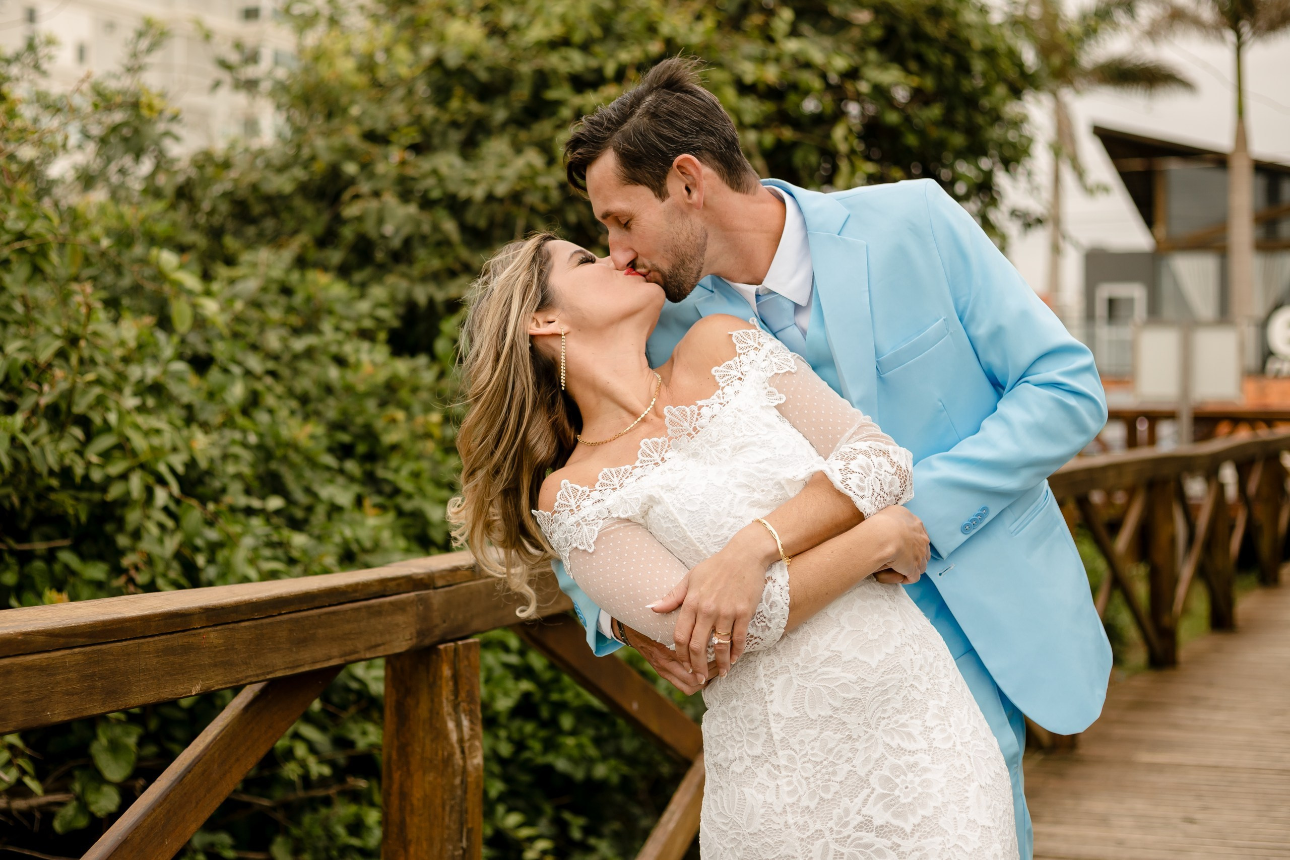 Fotógrafo de casamento em Navegantes; o noivo inclina a noiva para um beijo apaixonado na ponte de madeira durante ensaio externo na praia.