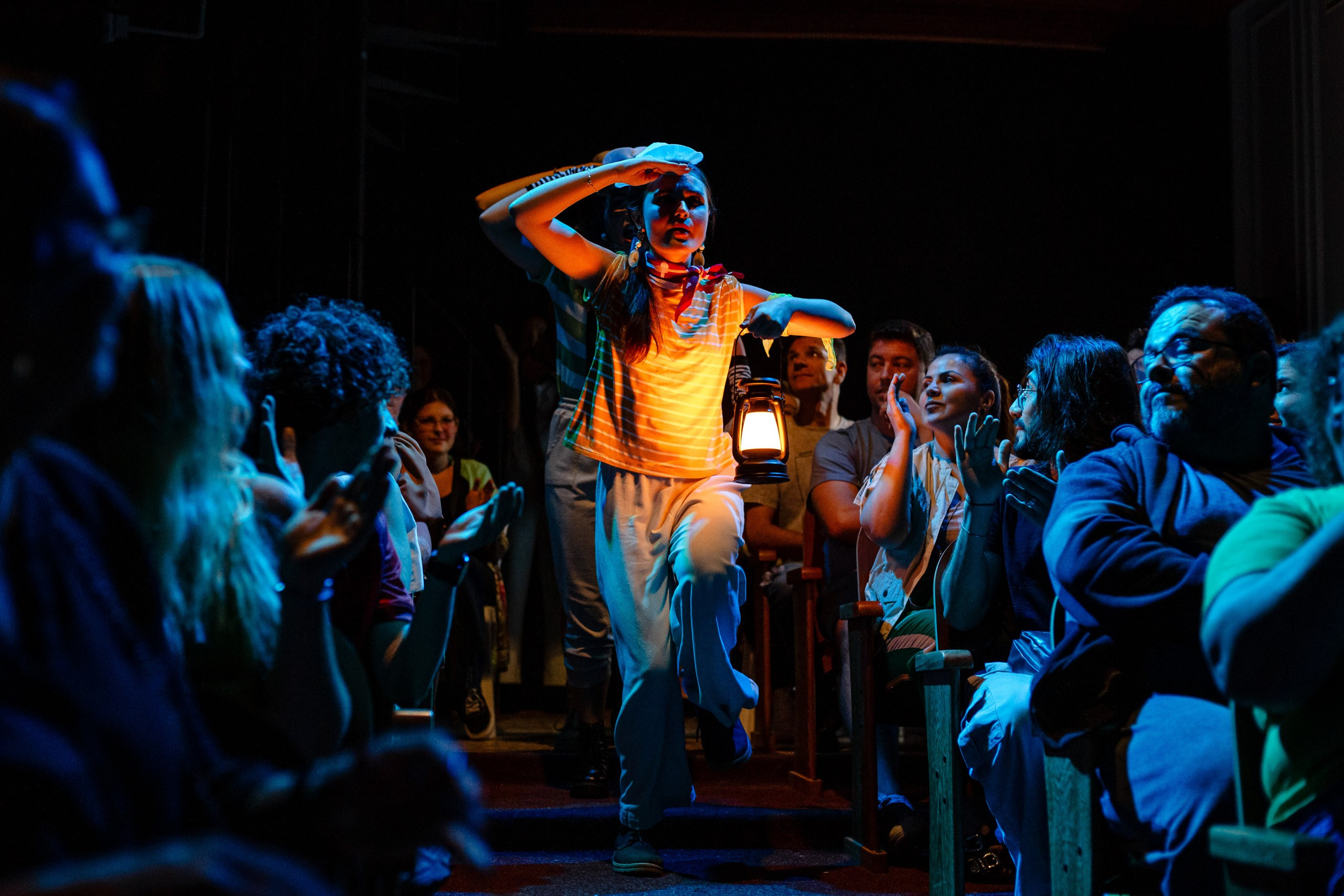 Apresentação teatral com grupo de náufragas andando em meio a plateia.