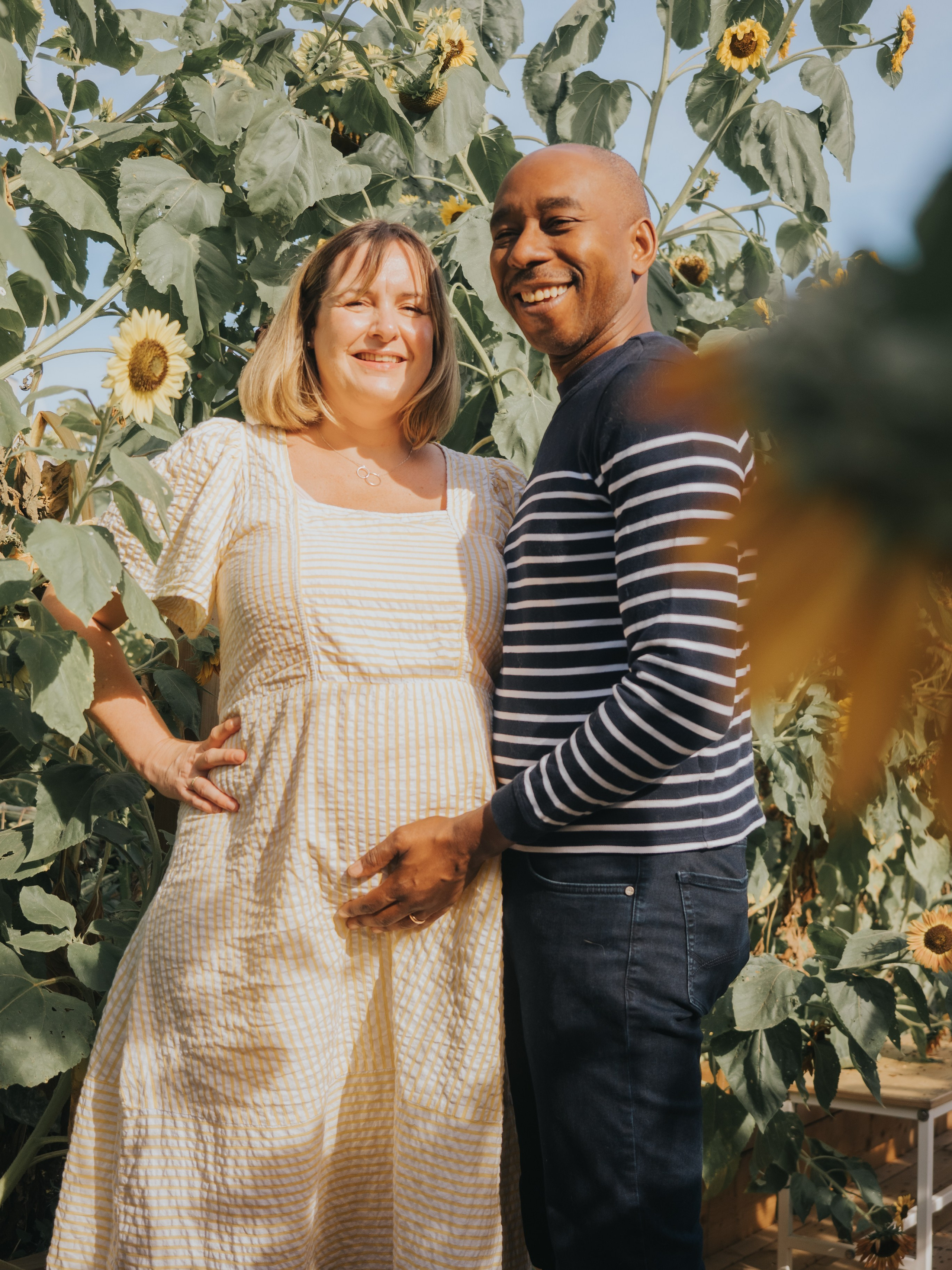 Couple avec femme enceinte entouré de tournesols.