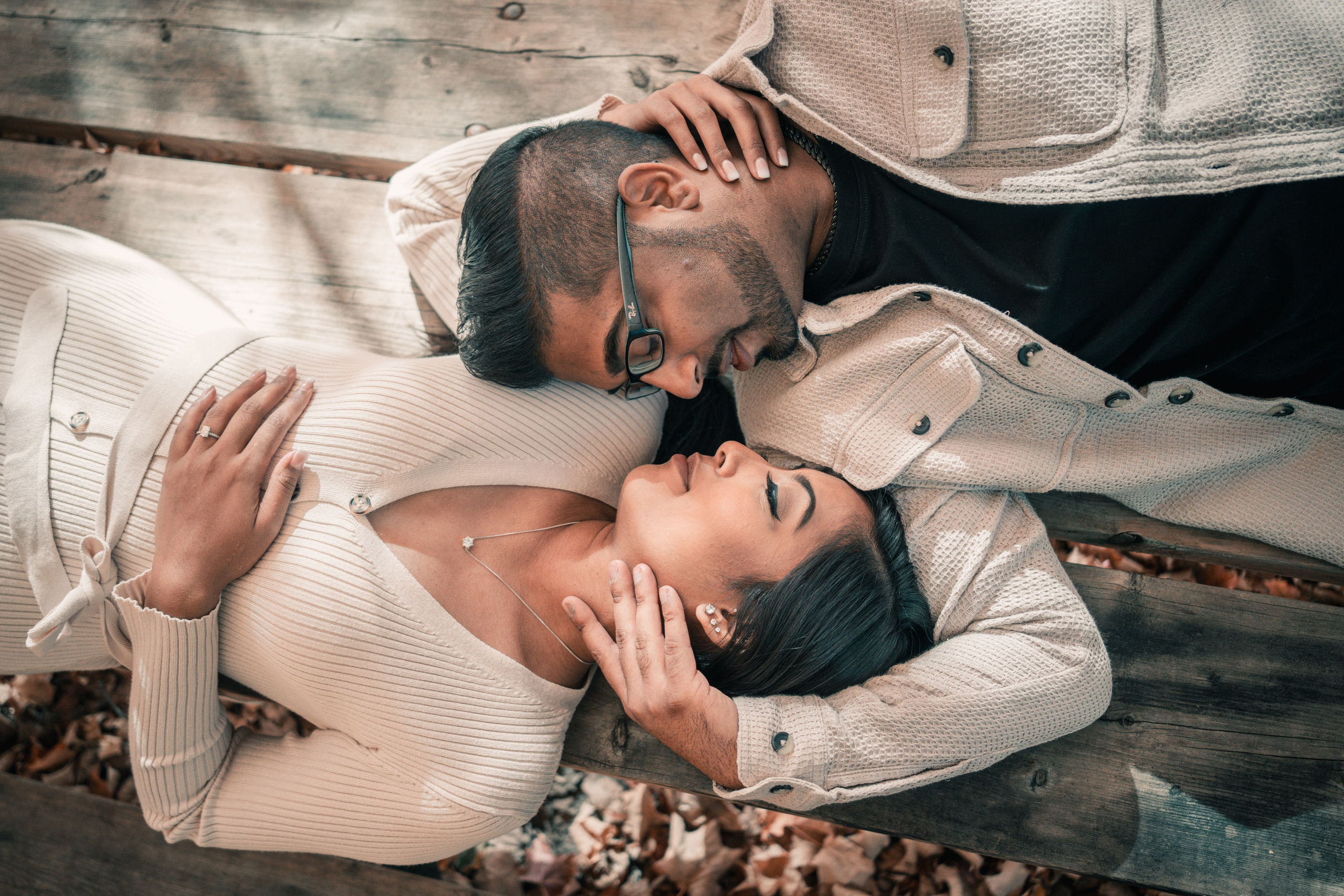 Engaged couple walking, lying down opposite each other in autumn park surrounded by trees and soft natural light during engagement.