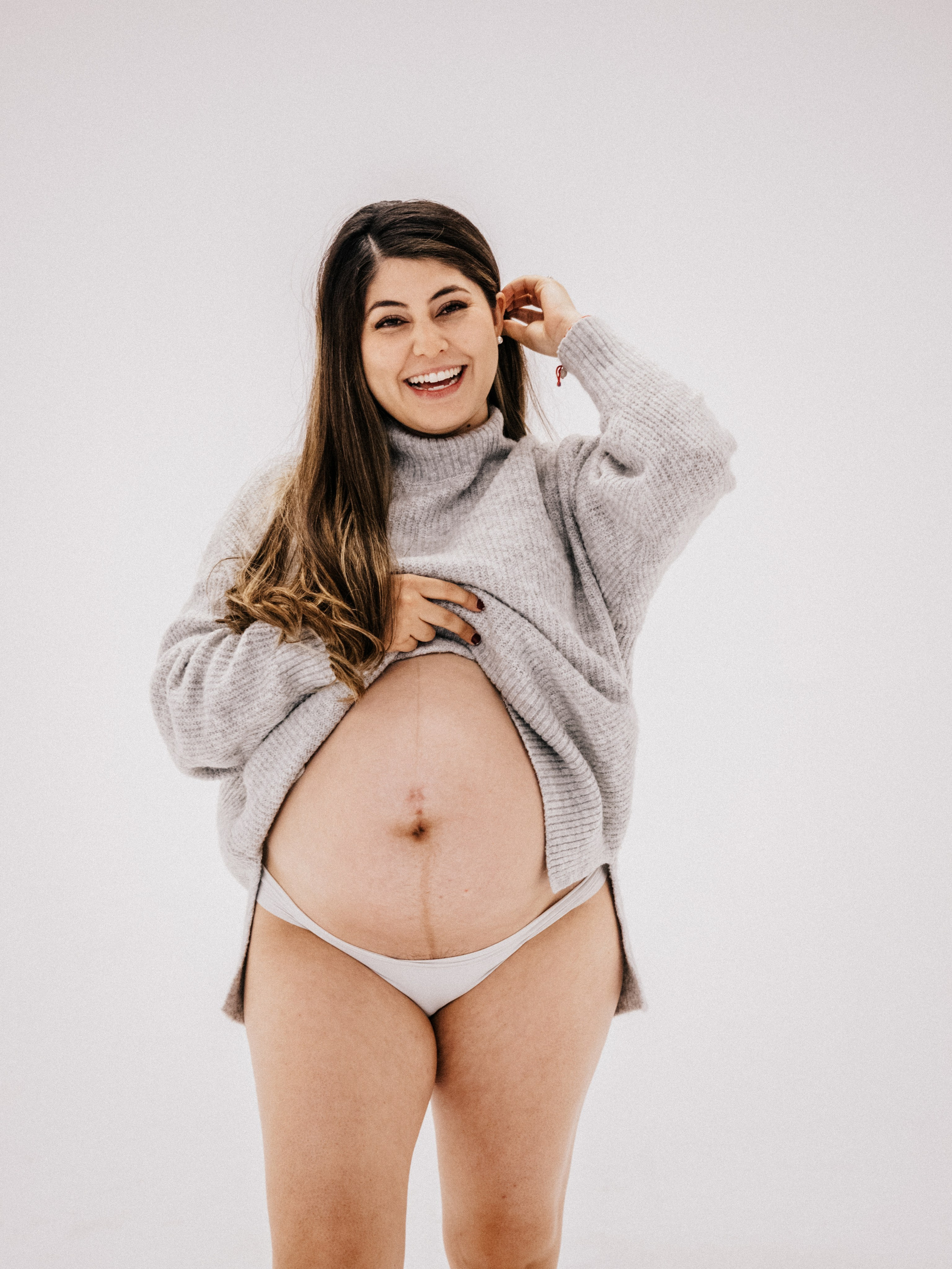 Femme enceinte qui sourit devant fond blanc dans un studio à Montréal.