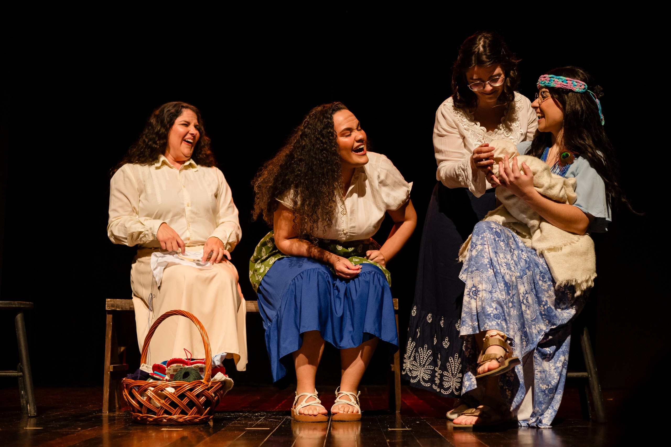 Apresentação teatral com grupo de mulheres sorrindo e olhando bebe.