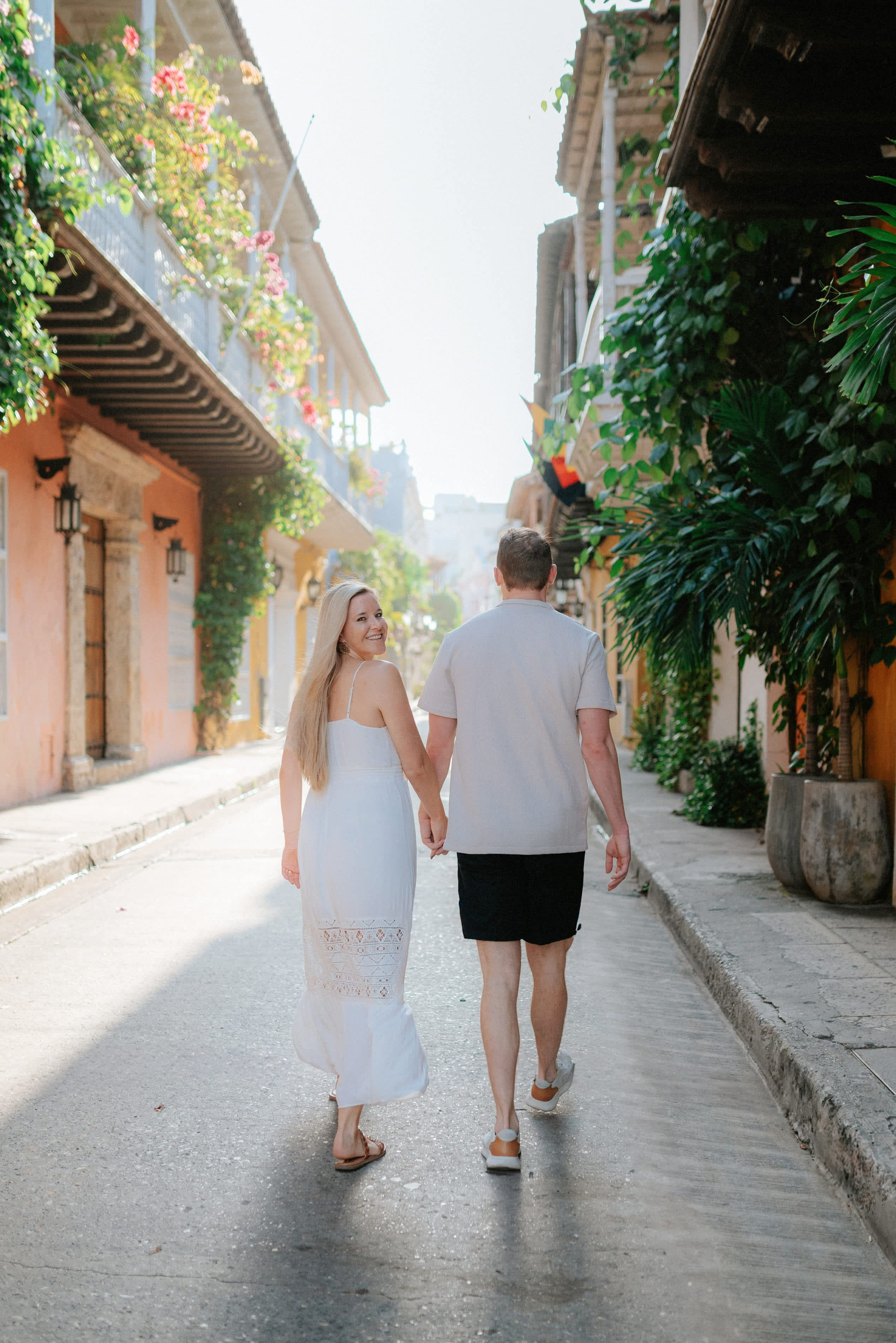 Couple walking down cobblestone street – “Bride and groom walking together on a charming cobblestone street in Cartagena, romantic wedding photoshoot in high quality