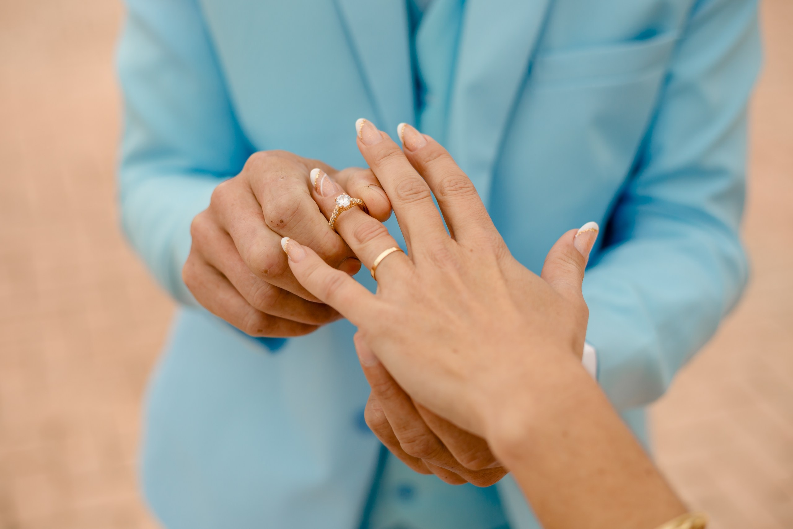 Fotógrafo de casamento em Navegantes; close detalhado das mãos do casal exibindo as alianças e o anel de compromisso durante ensaio externo na praia.