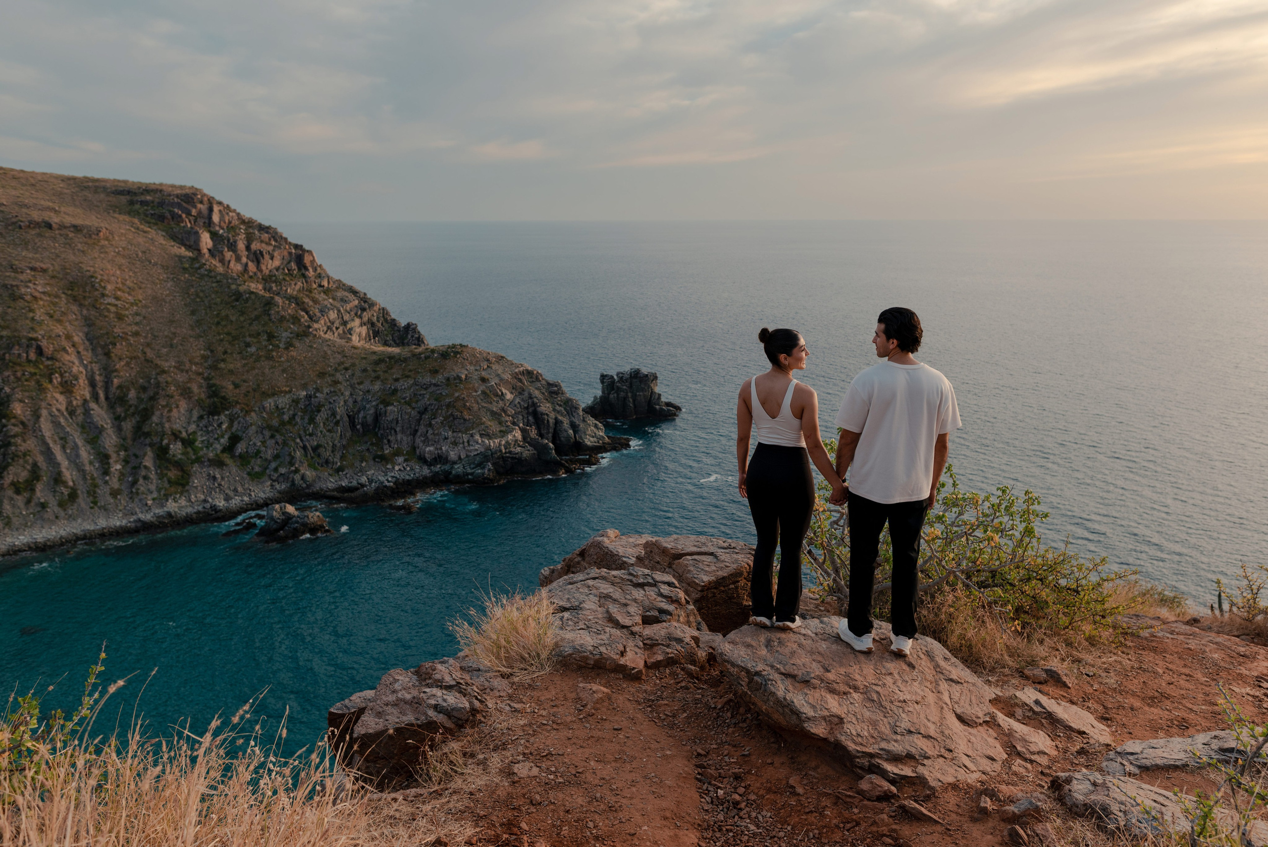 Couple standing at cliff edge with stunning turquoise cove at Punta Lobos, Todos Santos Baja California Sur
