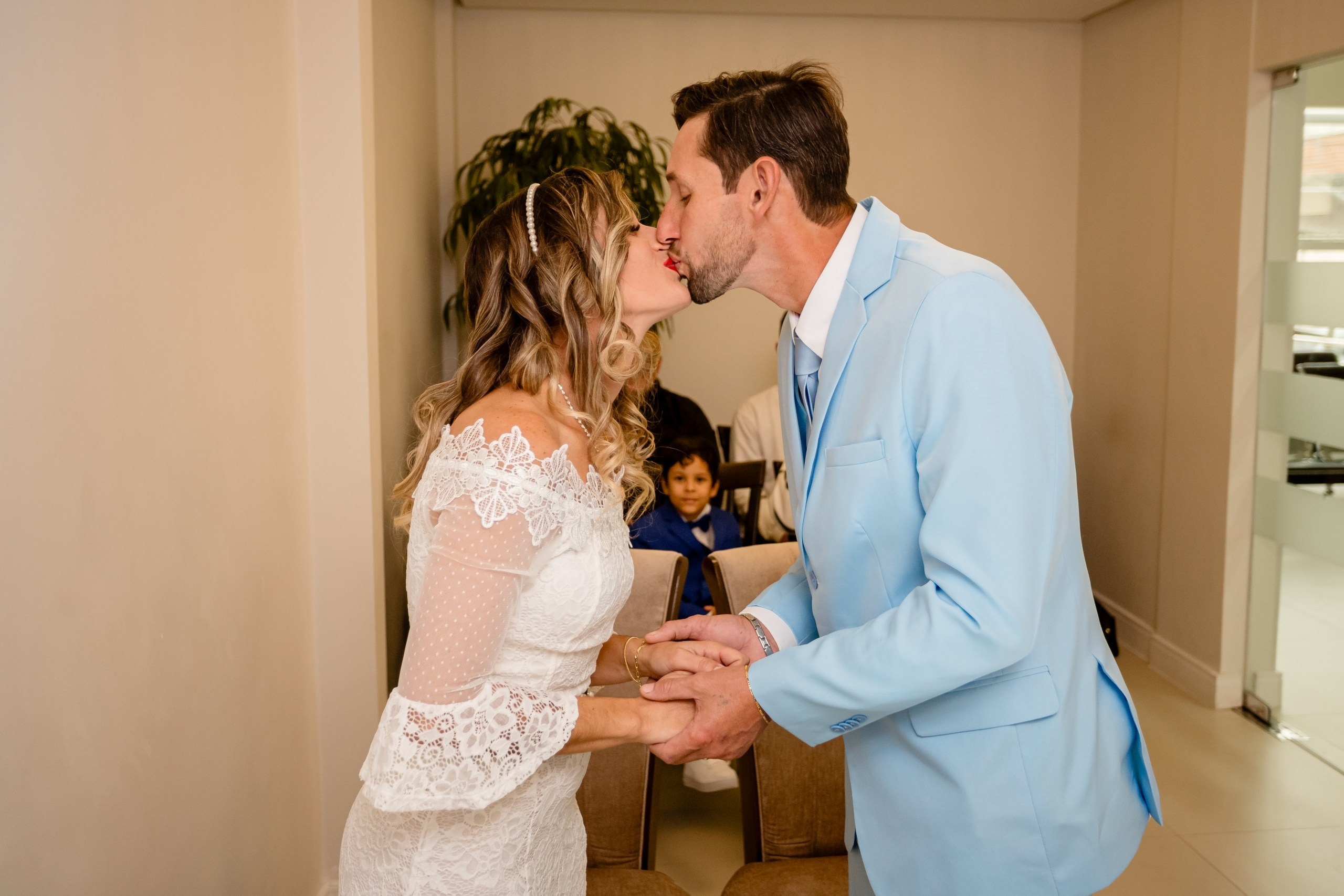 Fotógrafo de casamento civil em Navegantes; o recém-casado beijando a noiva de vestido branco durante a cerimônia, com uma criança ao fundo.