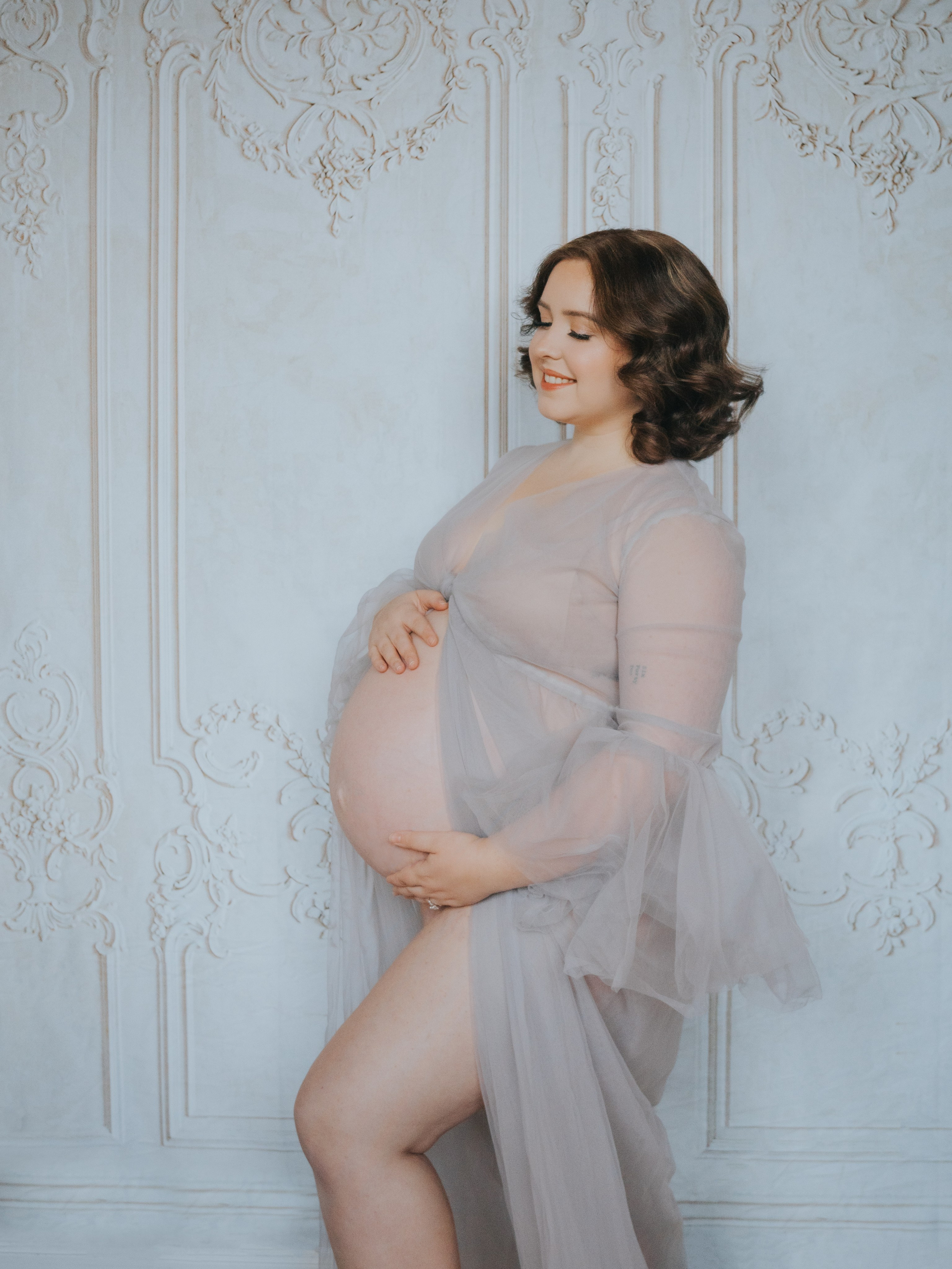 Femme enceinte devant un mur avec moulures.