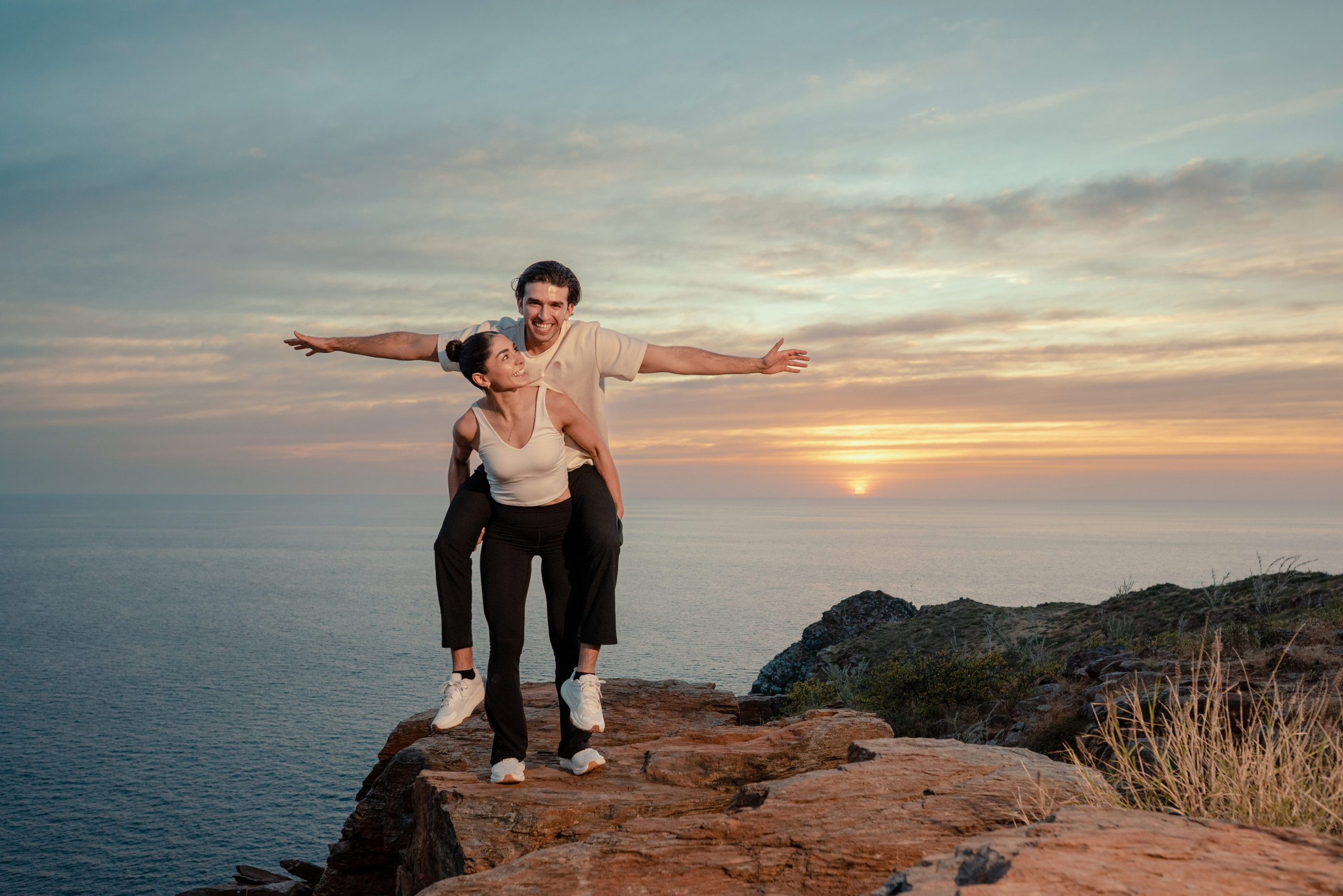Fiancée carrying groom in playful engagement moment on Punta Lobos cliffs, Todos Santos Mexico