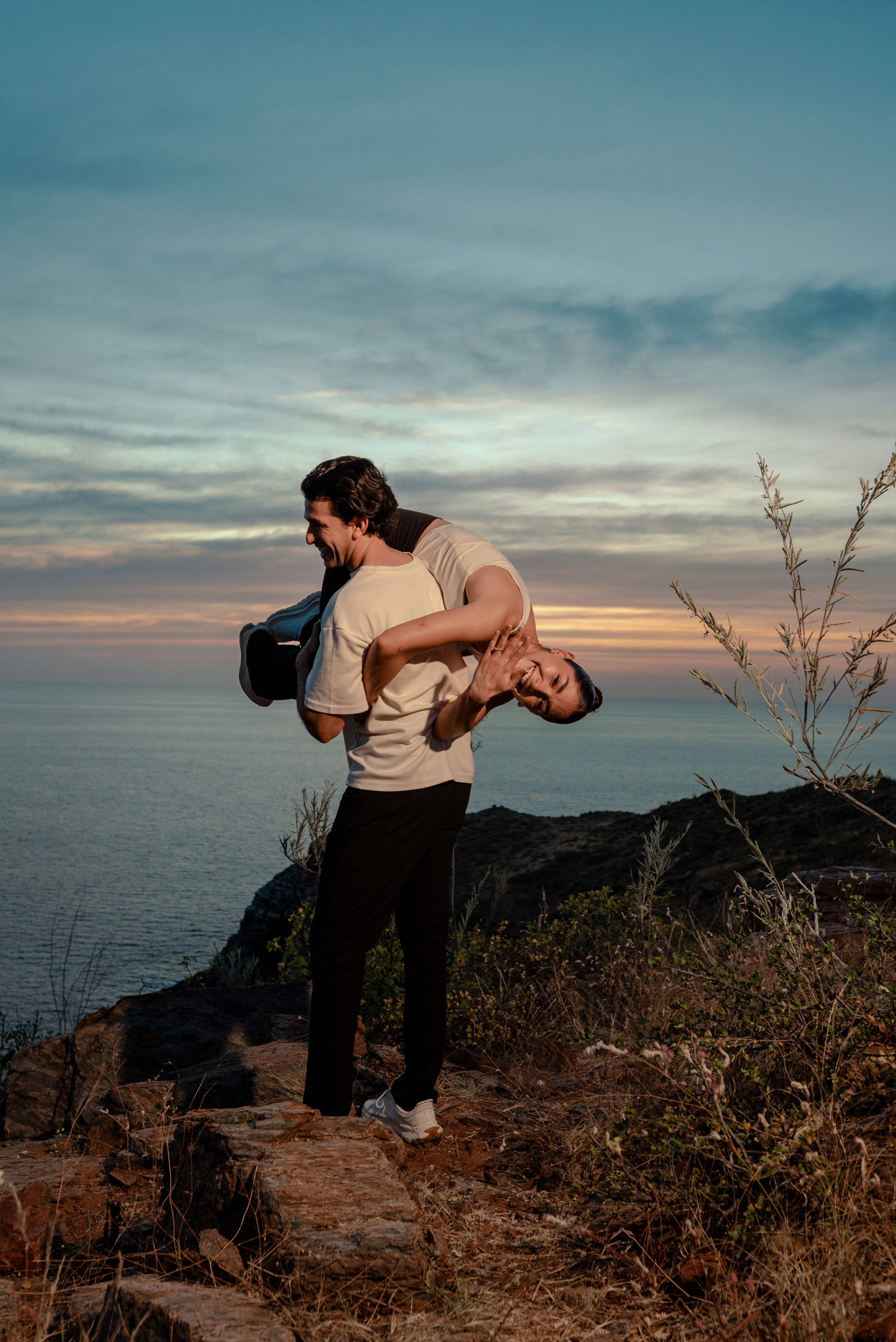 Groom lifting fiancée showing engagement ring on Punta Lobos cliffs with Pacific Ocean backdrop
