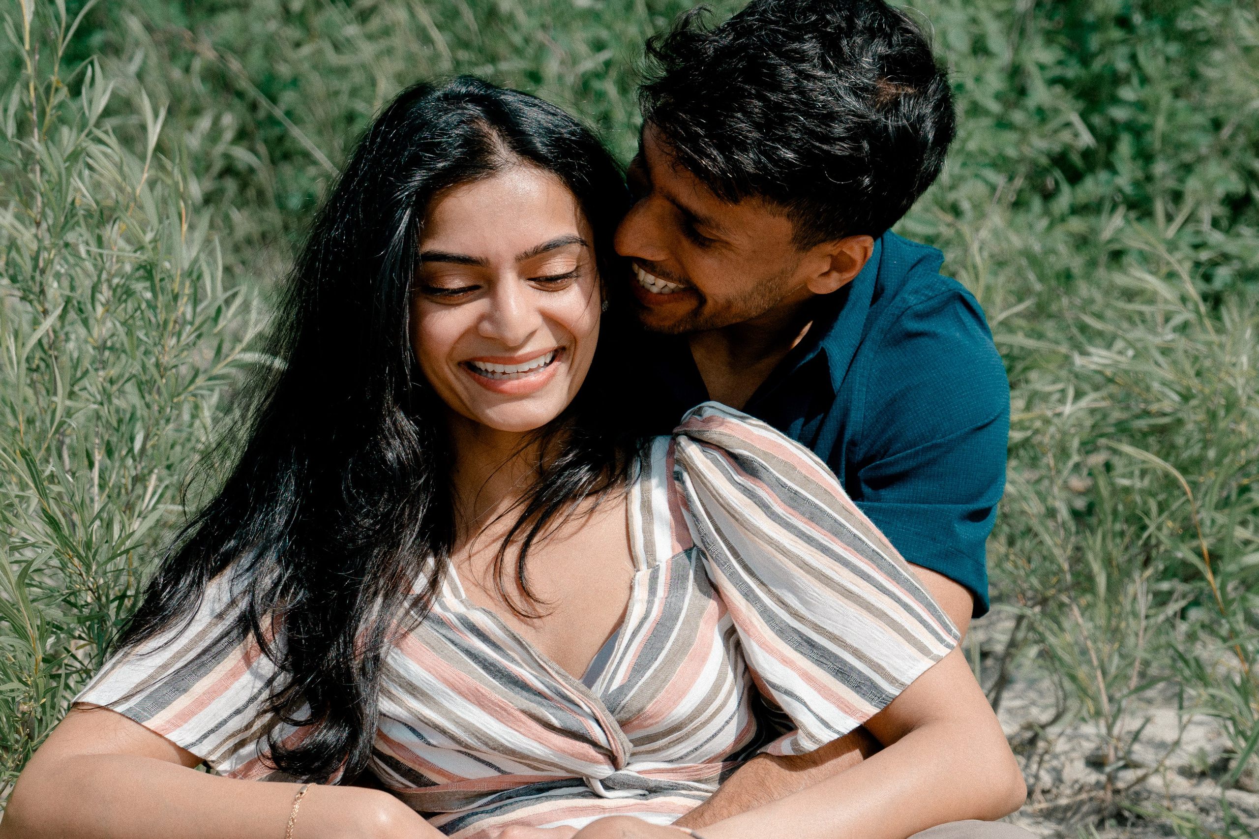 Joyful couple sitting in a sunny field, sharing a loving moment during their engagement photo session