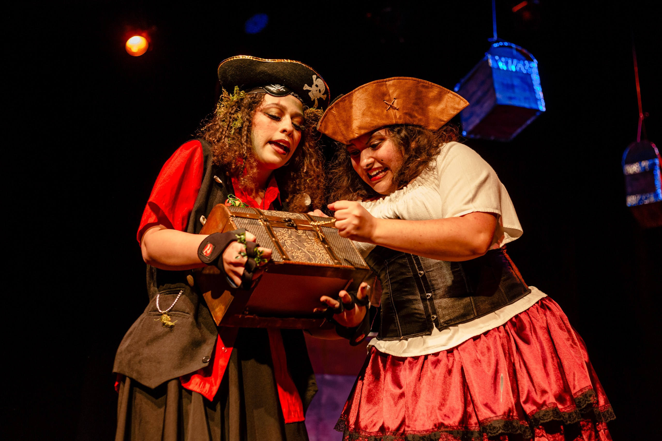 Apresentação teatral com duas piratas olhando baú de tesouro.