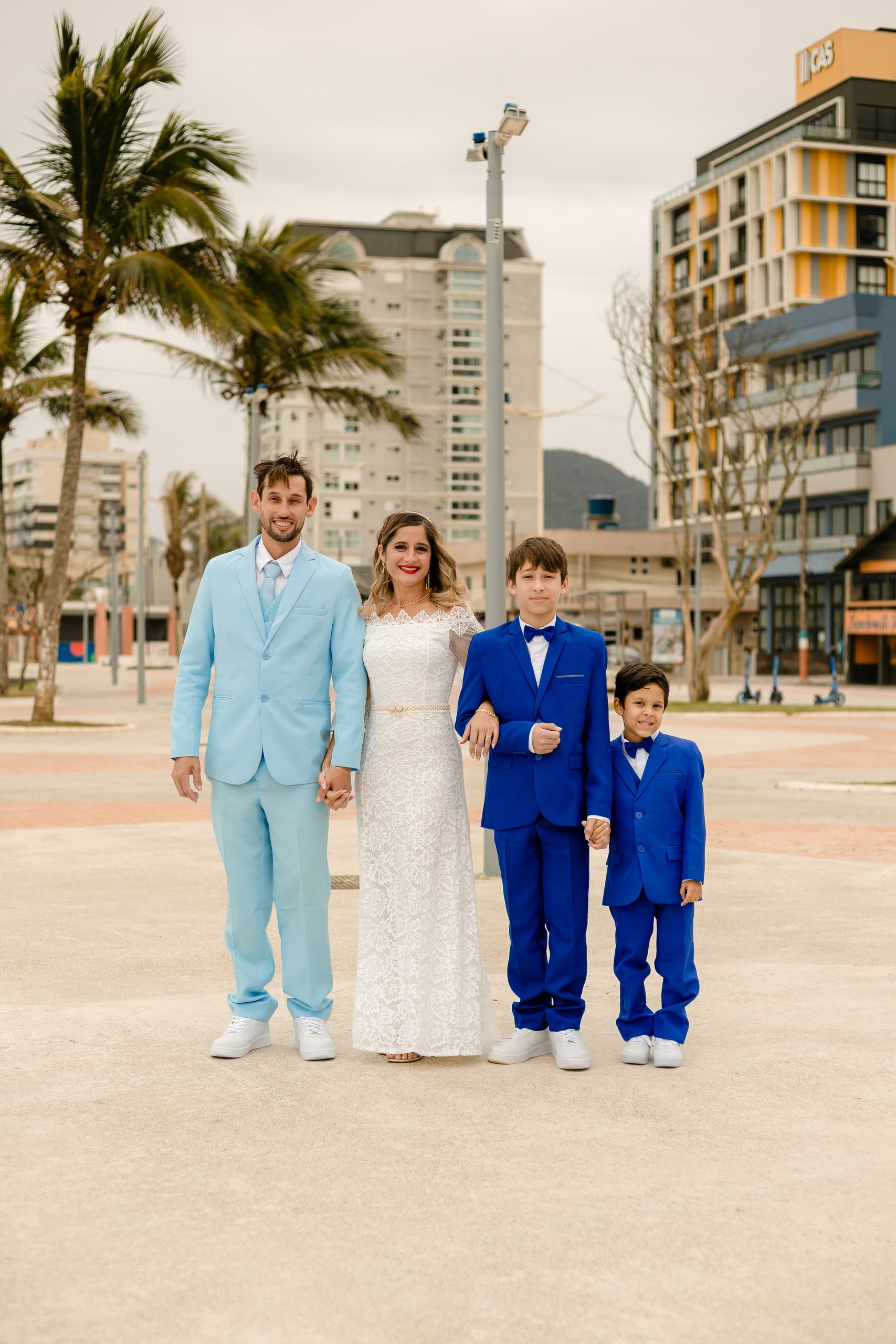 Fotógrafo de casamento em Navegantes; foto externa de família com os noivos e dois pajens ao ar livre na praça próxima à praia.