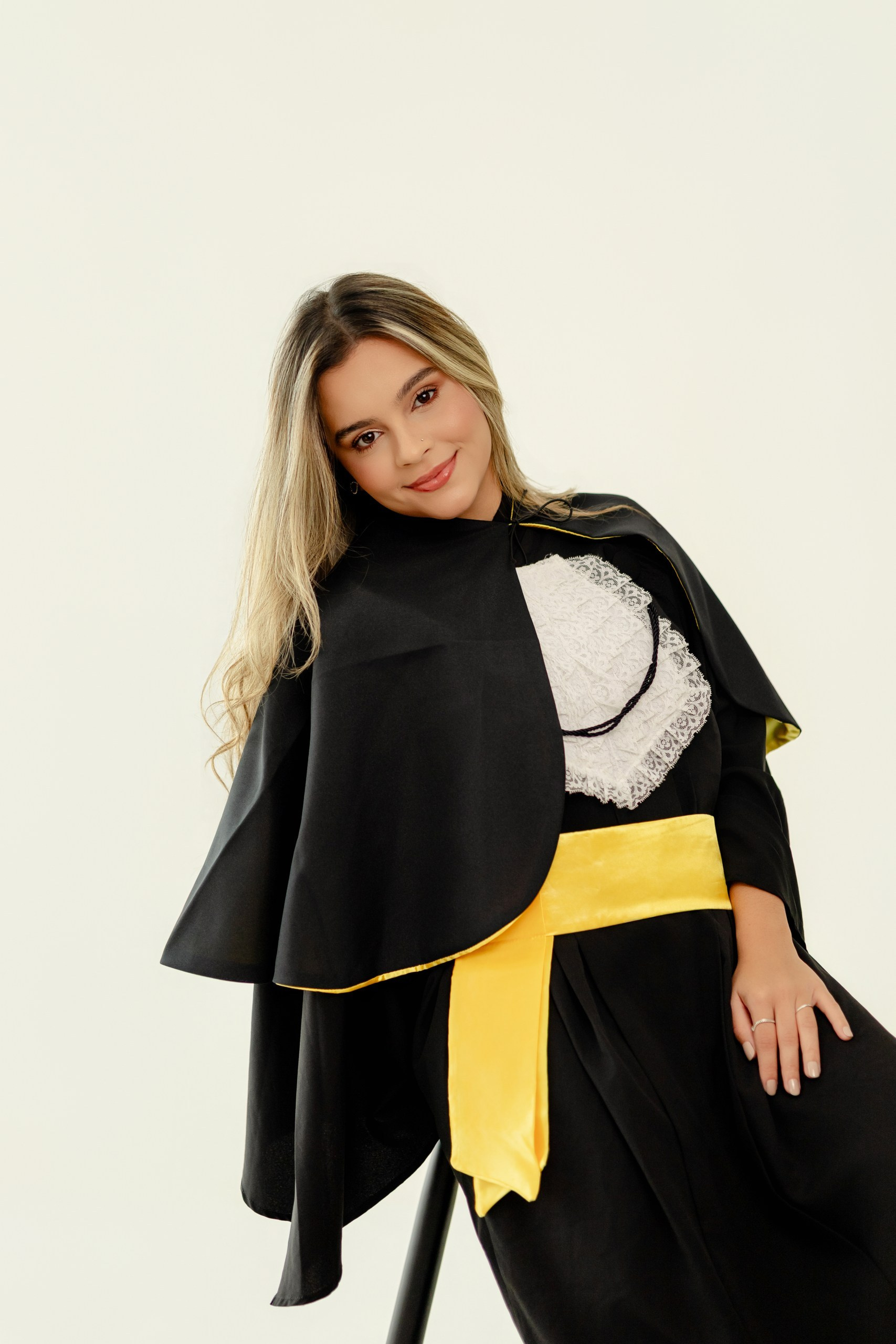 Fotografia de ensaio de formatura em Balneário Camboriú com formanda de farmácia sentada, sorrindo e vestindo beca com faixa amarela.