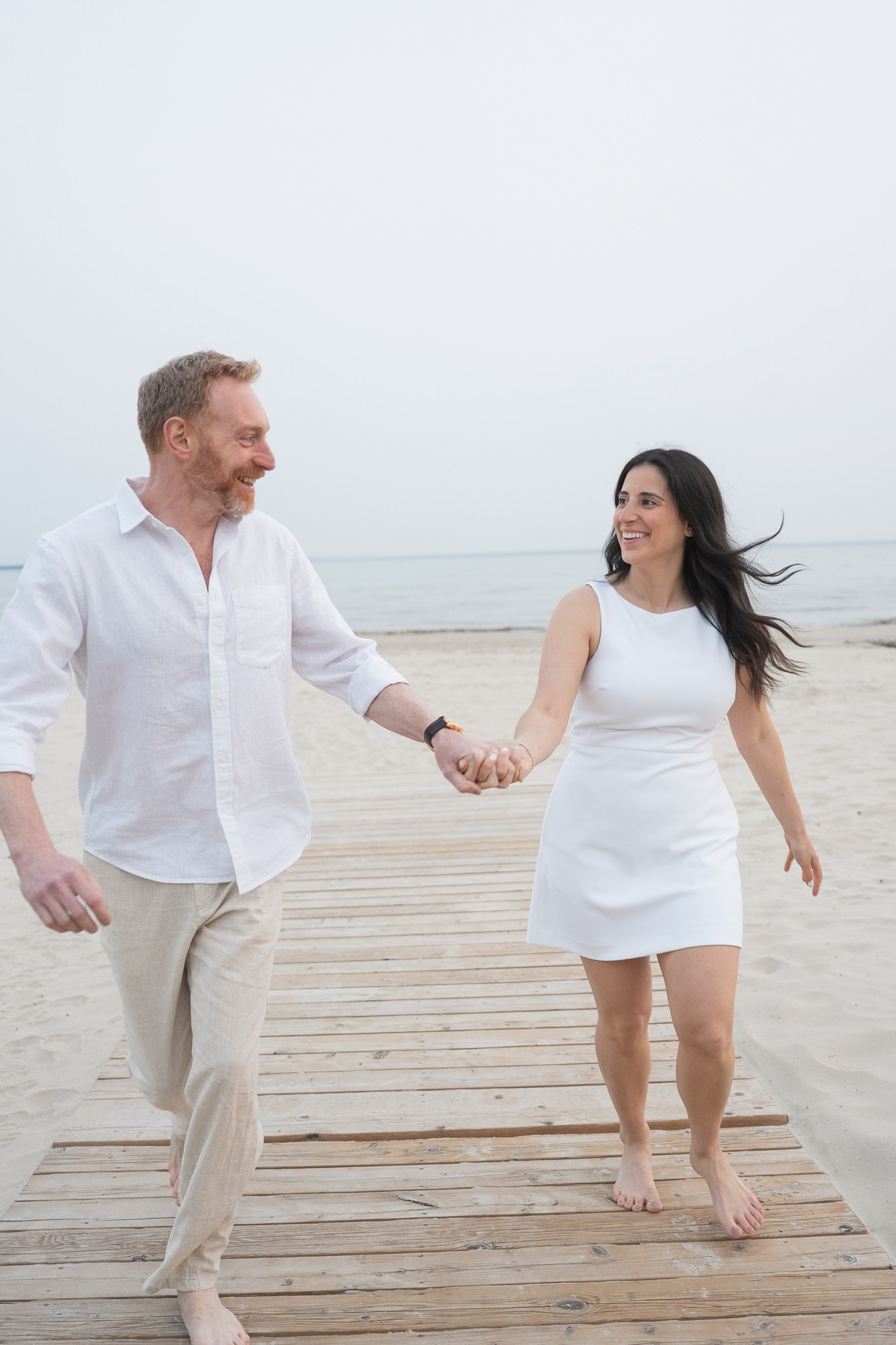 Couple walking hand in hand on a wooden boardwalk by the lake during their engagement photoshoot.