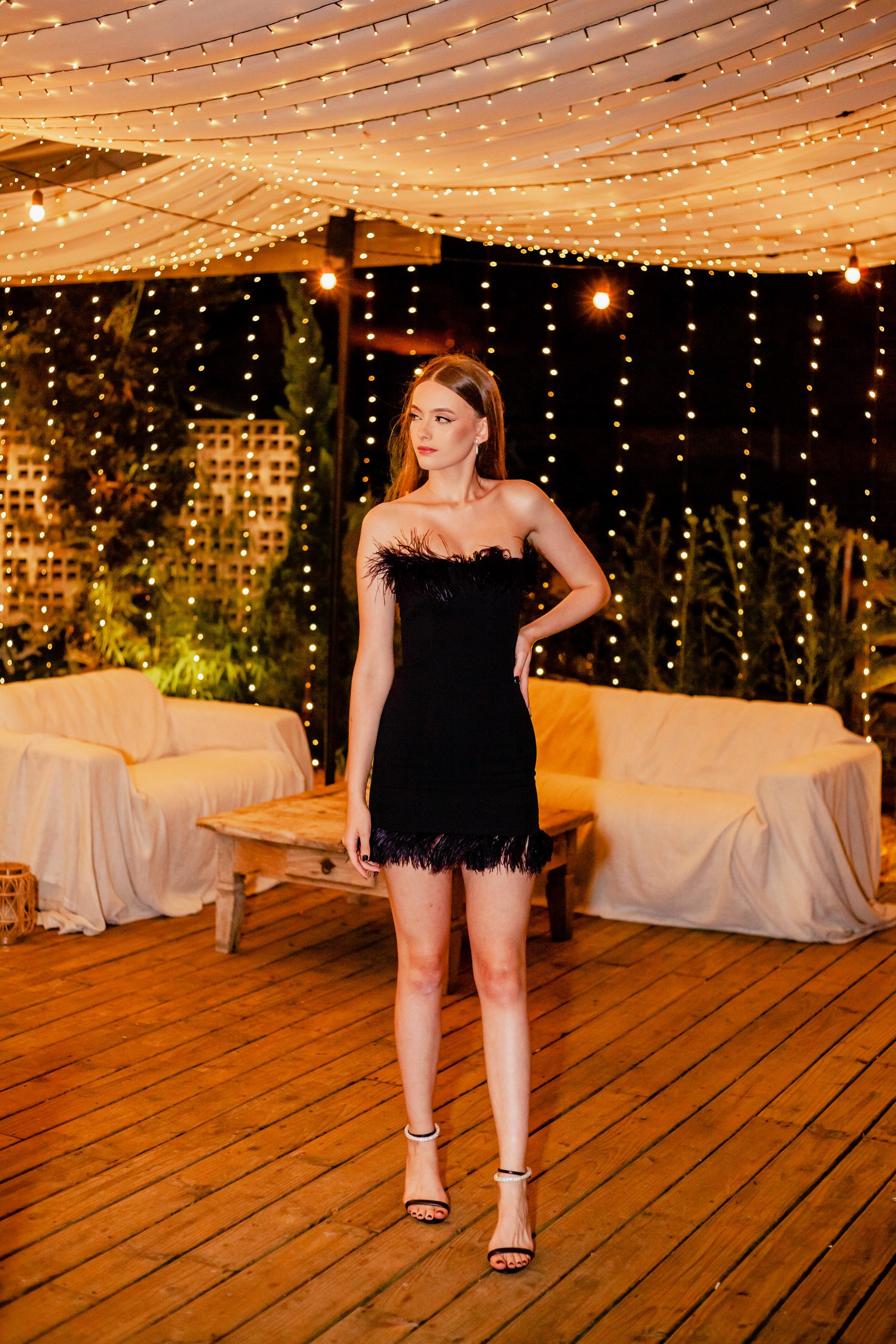 Fotógrafo festa de aniversário em Itajaí; retrato de corpo inteiro da aniversariante posando elegante em ambiente externo decorado com iluminação de luzes pendentes.