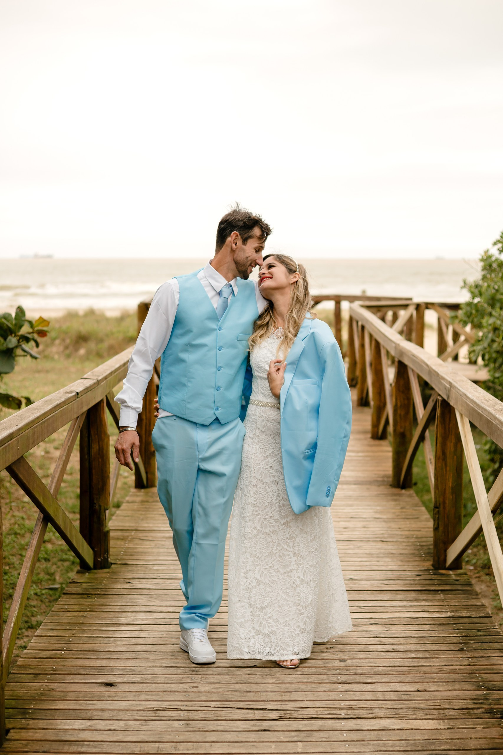 Fotógrafo de casamento em Navegantes; o casal caminha sorridente sobre a ponte de madeira com a paisagem natural ao fundo durante o ensaio externo.