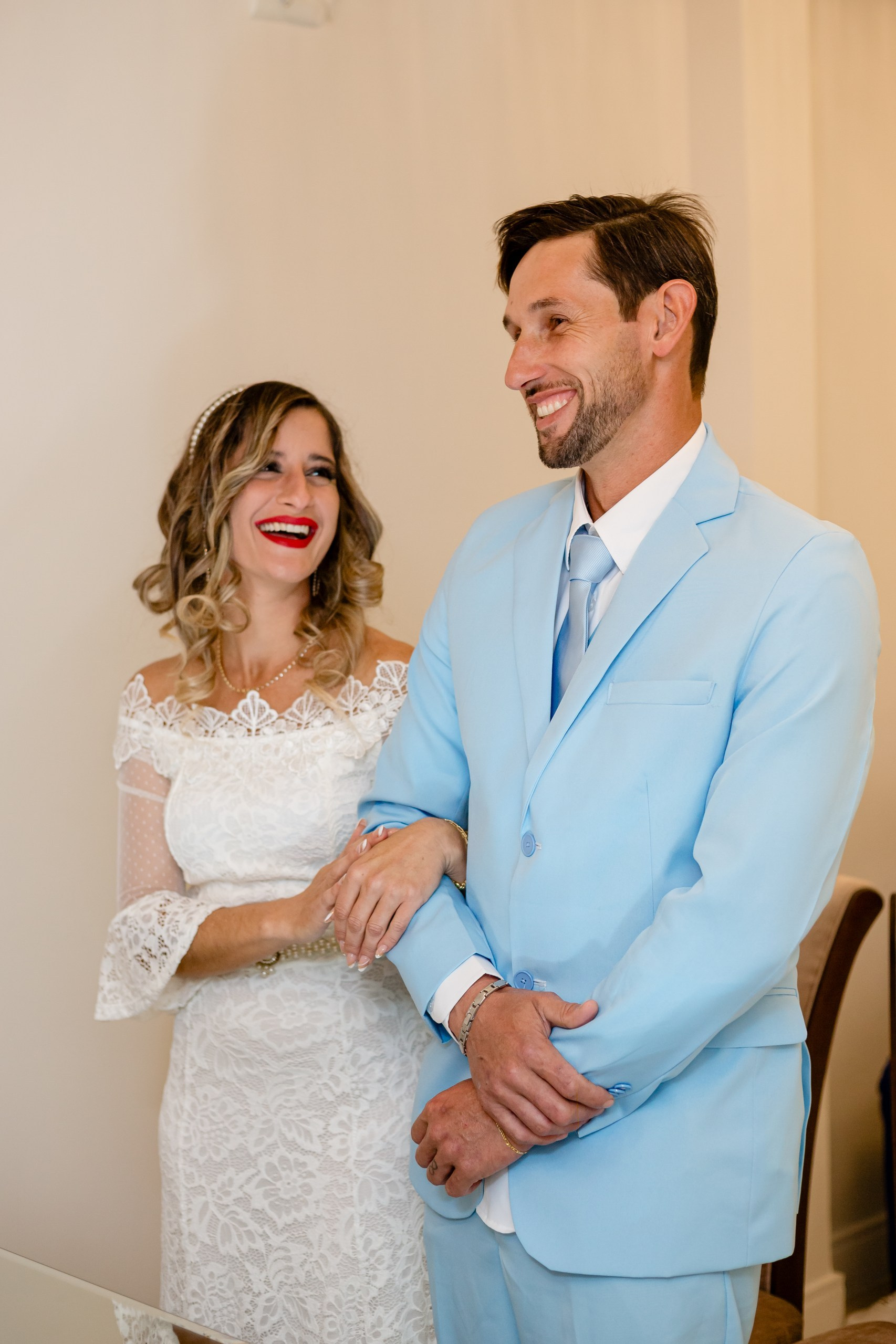 Fotógrafo de casamento civil em Navegantes; a noiva sorrindo alegremente ao lado do noivo de terno azul claro durante a cerimônia no cartório.
