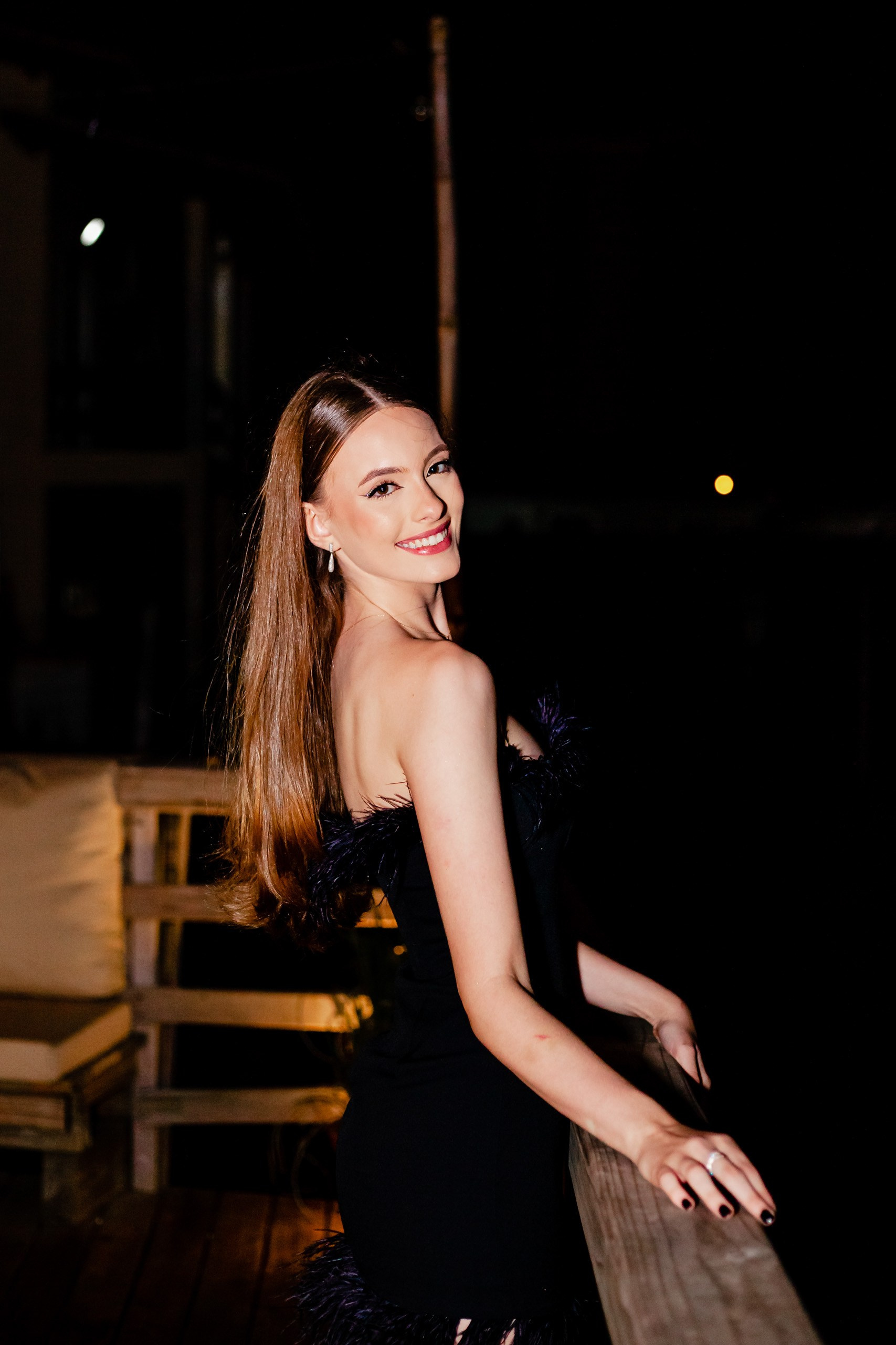 Fotógrafo festa de aniversário em Itajaí; retrato lateral sorridente da aniversariante com vestido preto elegante durante comemoração noturna ao ar livre.