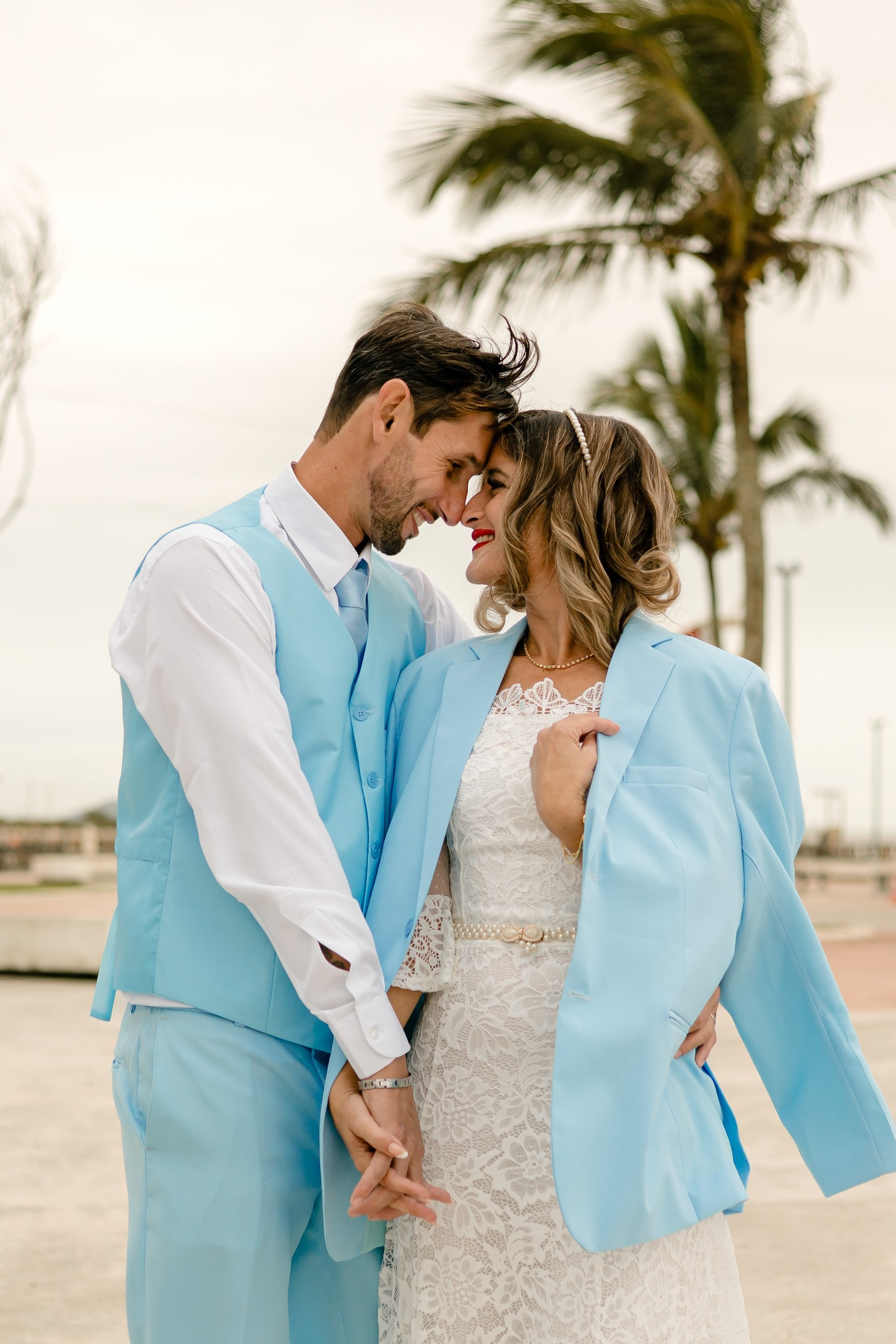 Fotógrafo de casamento em Navegantes; o casal de mãos dadas, com os rostos próximos e sorridentes, tendo coqueiros e a paisagem da praia ao fundo durante ensaio romântico.