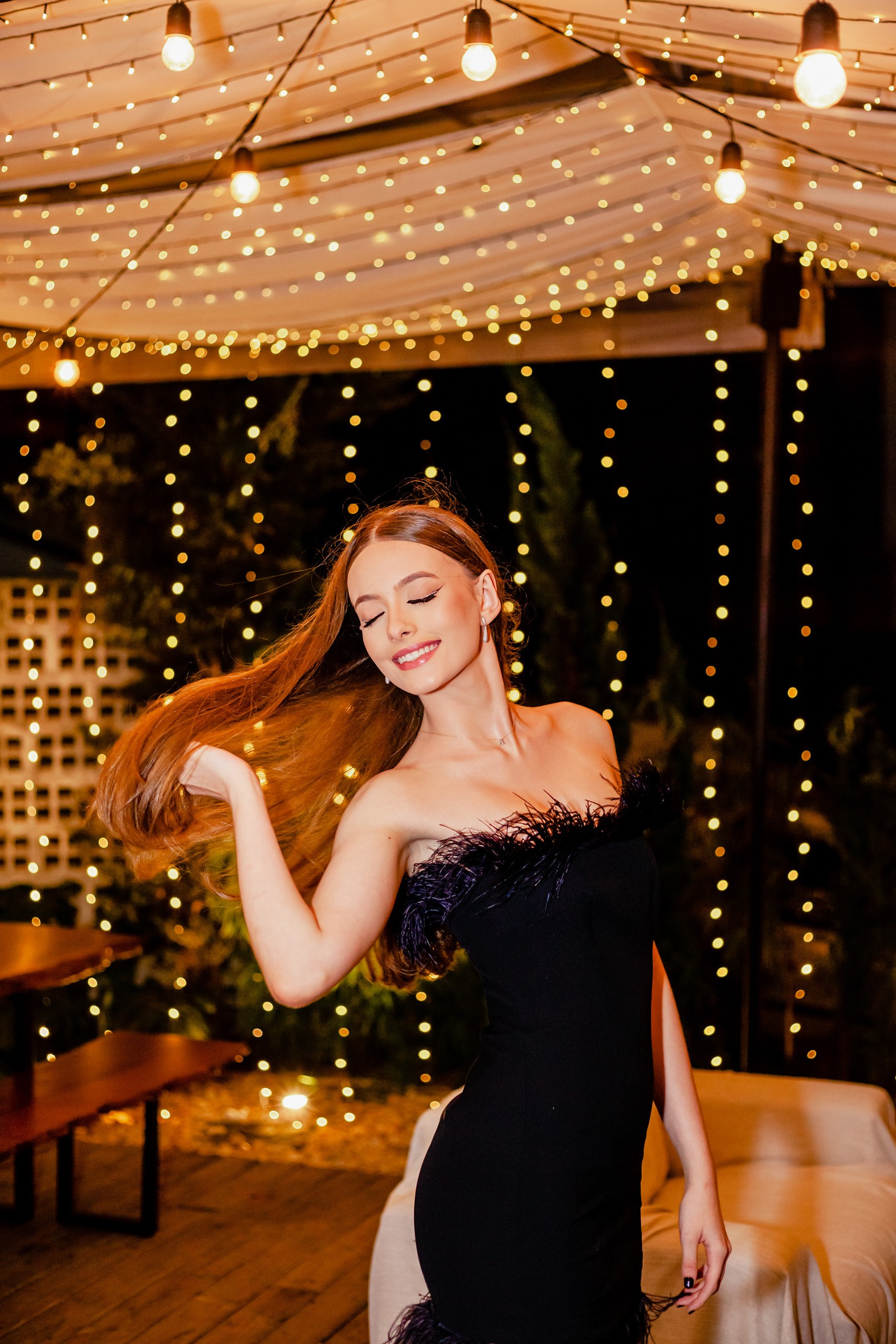 Fotógrafo festa de aniversário em Itajaí; retrato dinâmico e alegre da aniversariante a mover o cabelo com elegância, tendo ao fundo a iluminação mágica de luzes suspensas.