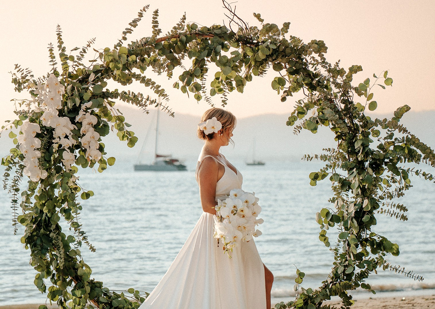 Bride standing beneath a wedding arch at sunset on a tropical beach