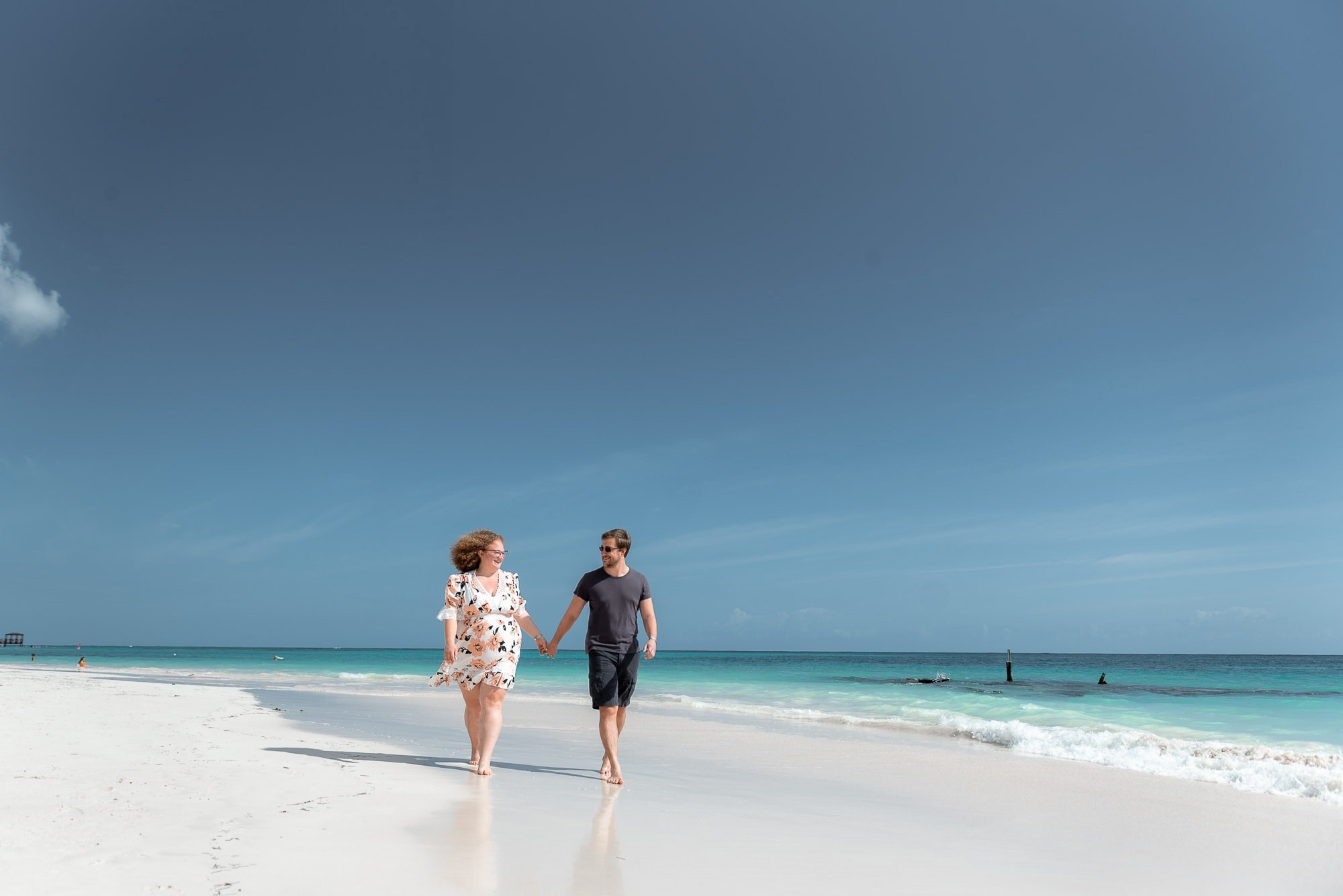 Pregnant woman with curly hair and her husband walking on Bavaro Beach during a photoshoot