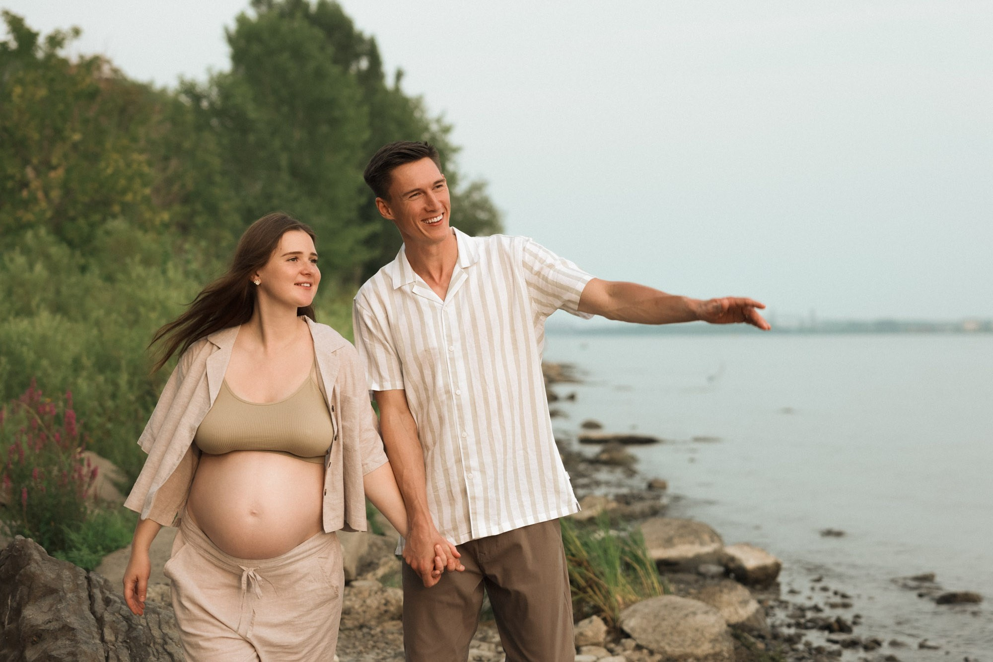 Expecting couple walking hand in hand along the shoreline in Greater Montreal
