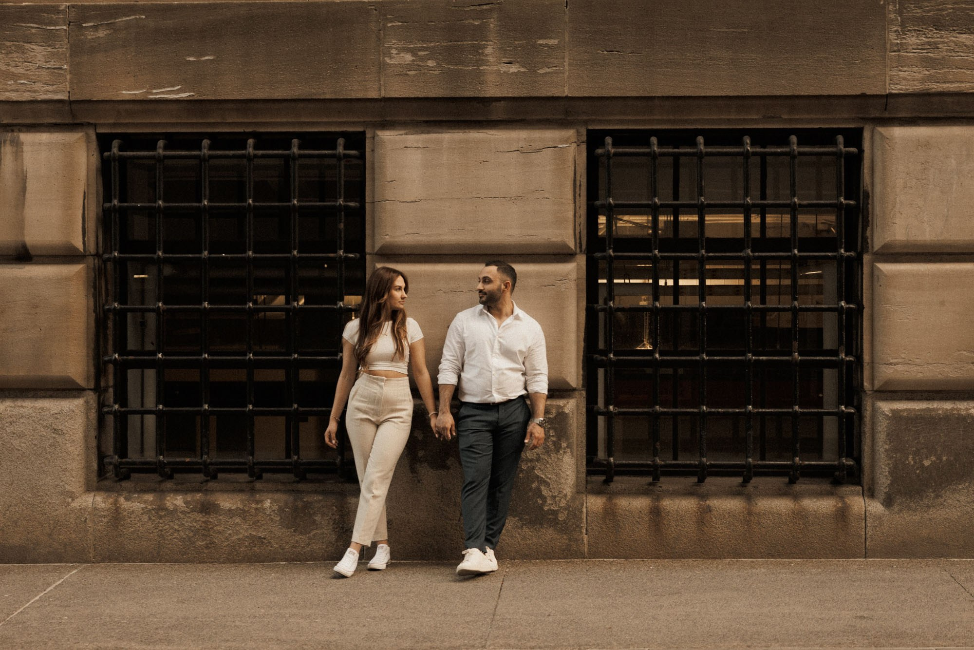 Couple walking hand in hand past a stone building in Montreal