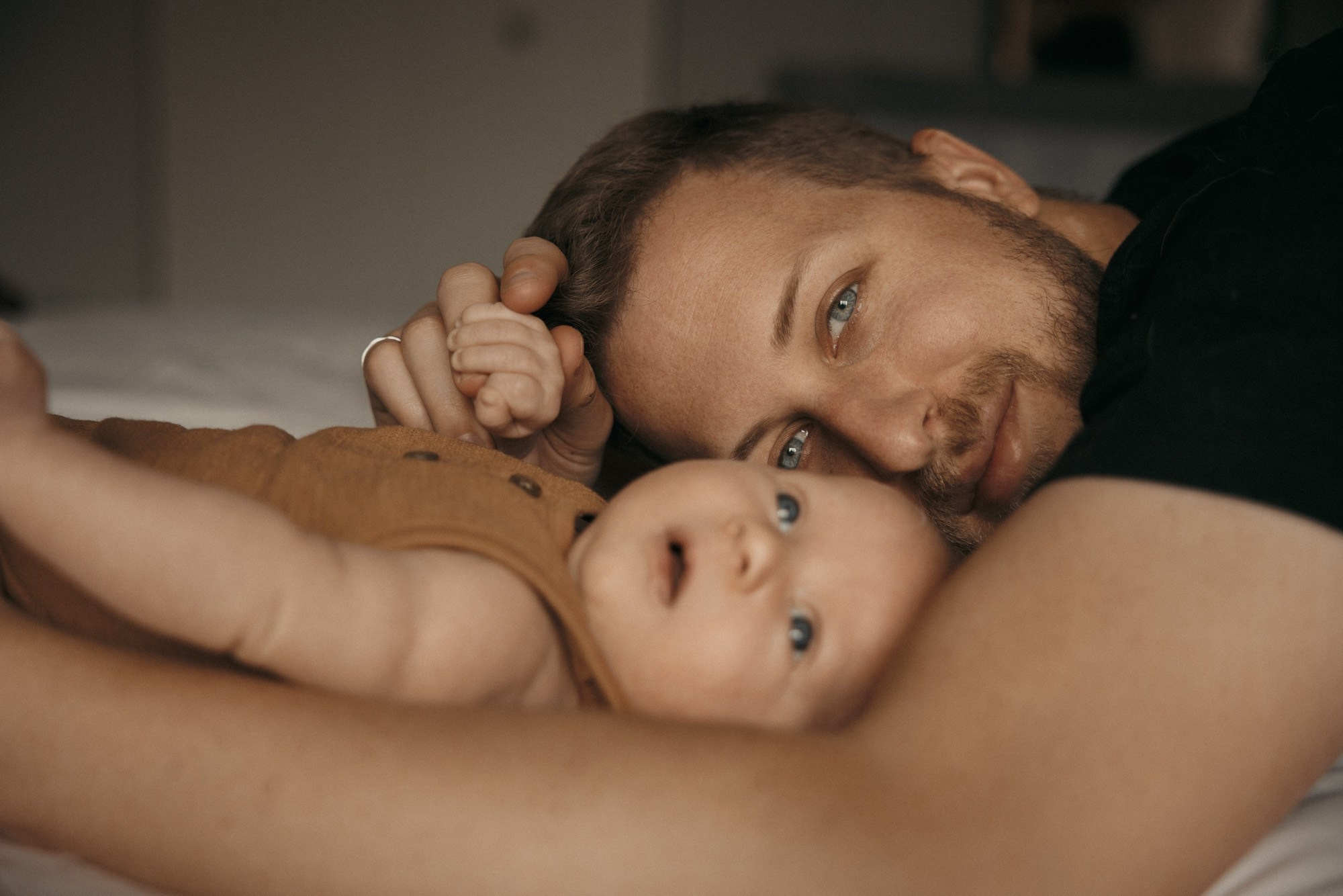 Père allongé avec son nouveau-né lors d’une séance photo naturelle à domicile
