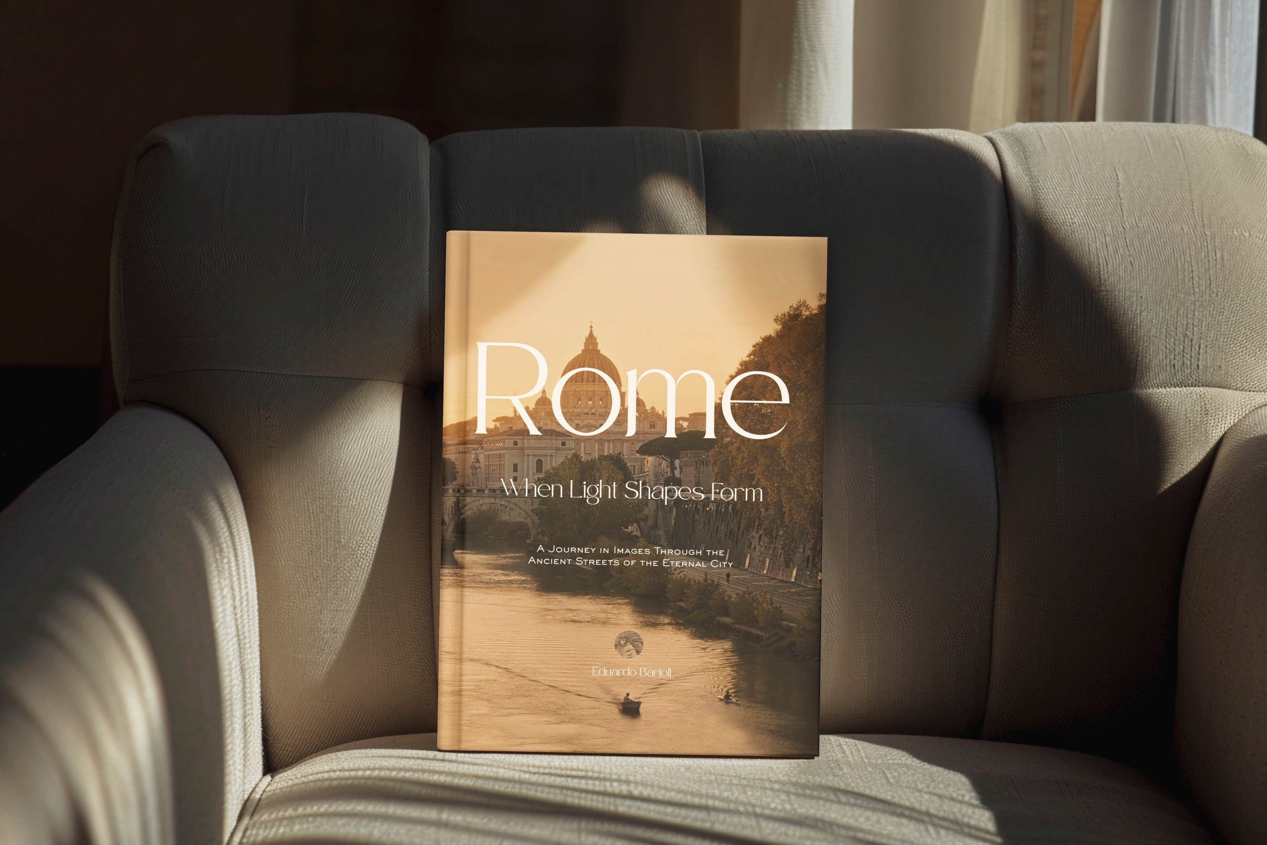 Rome, Italy – Photography Book – Rome — When Light Shapes Form – Hardcover photography book displayed on an armchair, featuring the cover with a sunset view of St. Peter's Basilica and the Tiber River – Eduardo Bartoli Photography