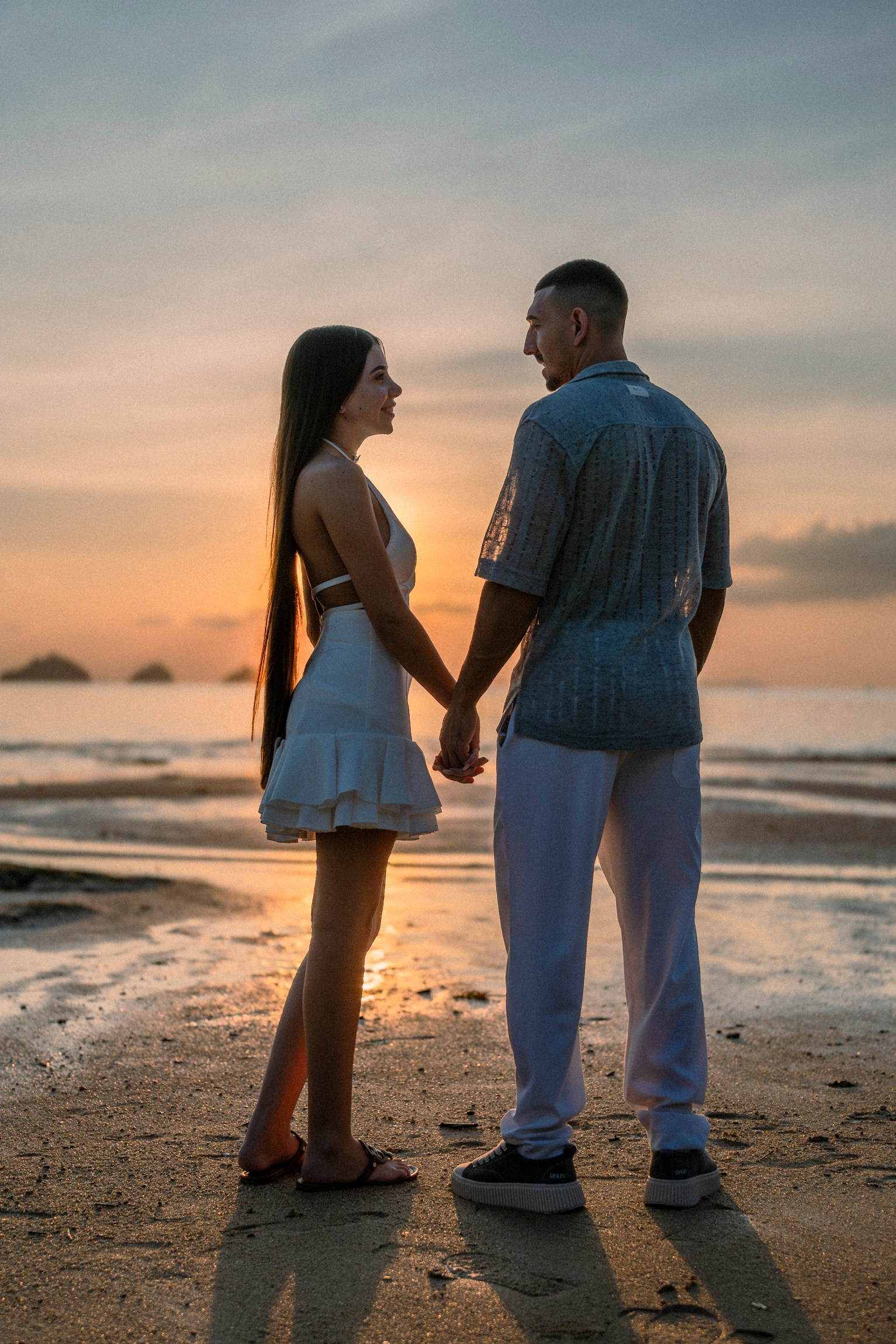 Romantic couple walking together along a Pattaya beach at sunset after their marriage proposal.