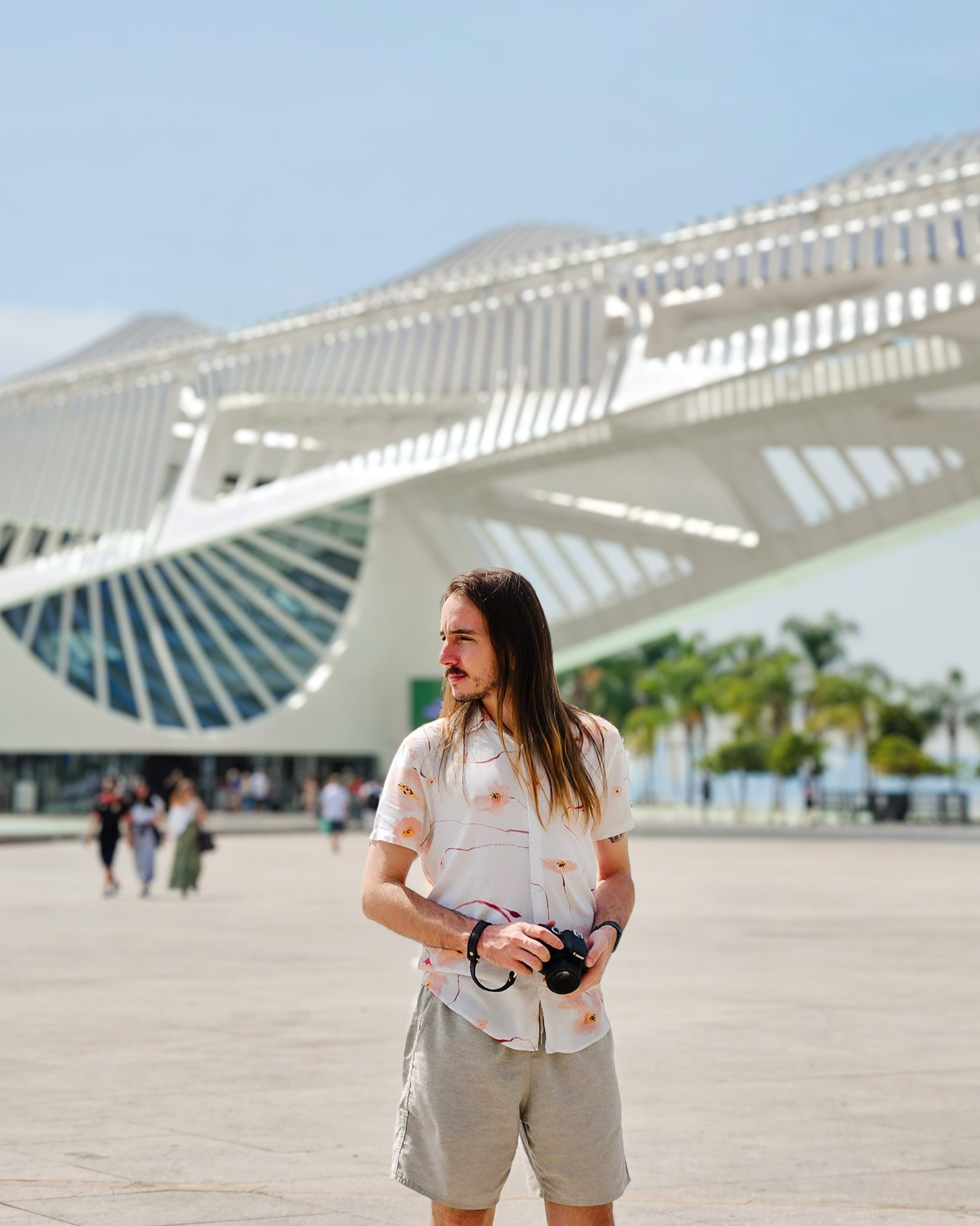 Fotógrafo segurando câmera em praça aberta com a arquitetura do Museu do Amanhã ao fundo