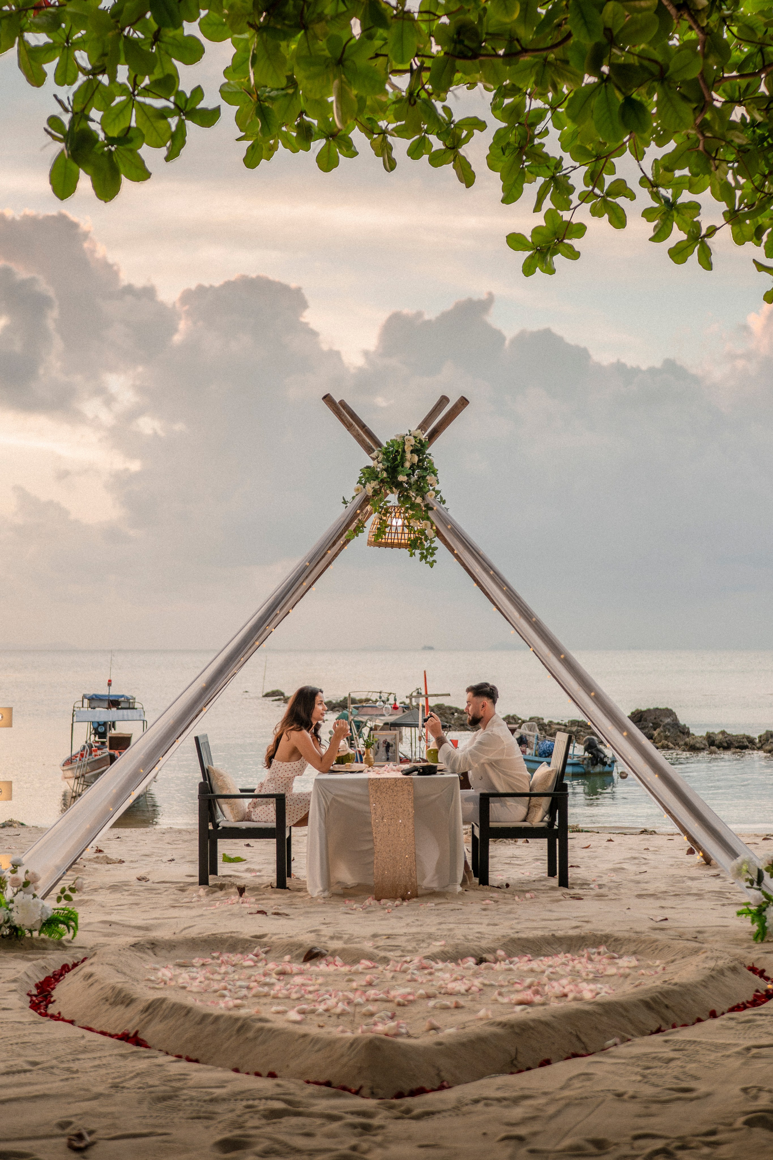 Romantic beach dinner setup in Pattaya with a teepee, candles, rose petals and a seaside table for two.