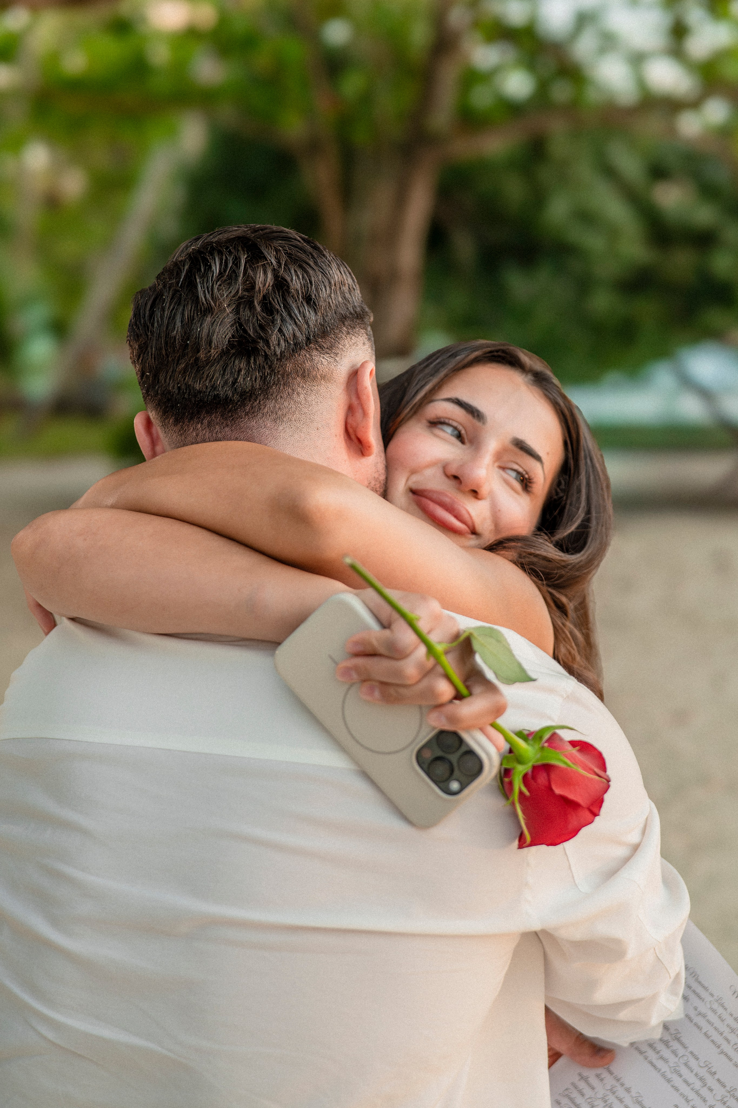 Happy couple embracing after a romantic marriage proposal on the beach in Pattaya, with a red rose in hand.