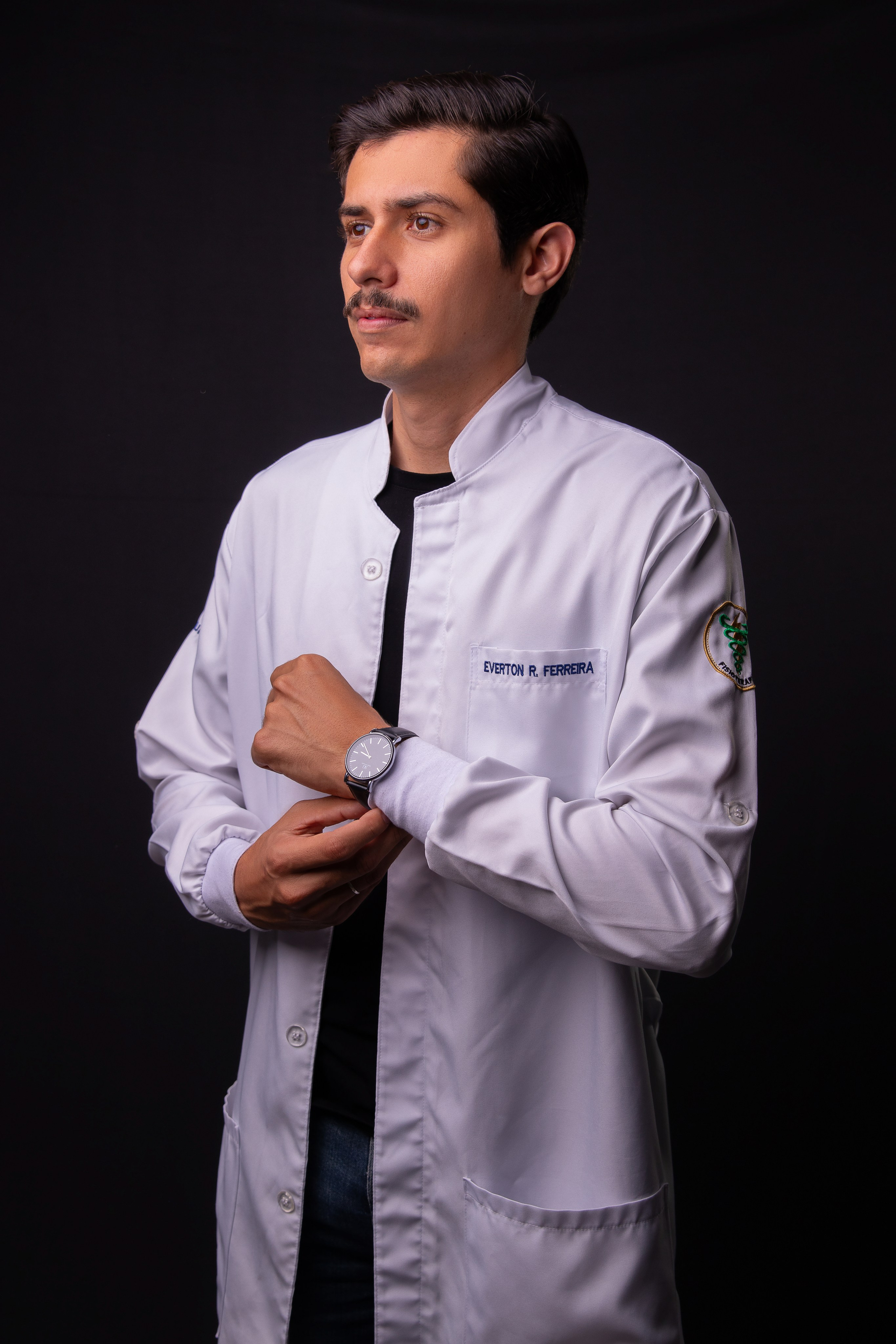 Retrato profissional em estúdio de fisioterapeuta vestindo jaleco branco em pose corporativa.