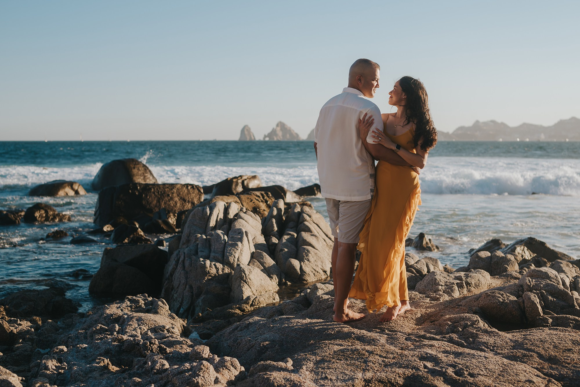 Maternity couple embracing at sunset with Cabo San Lucas Arch in backgroud