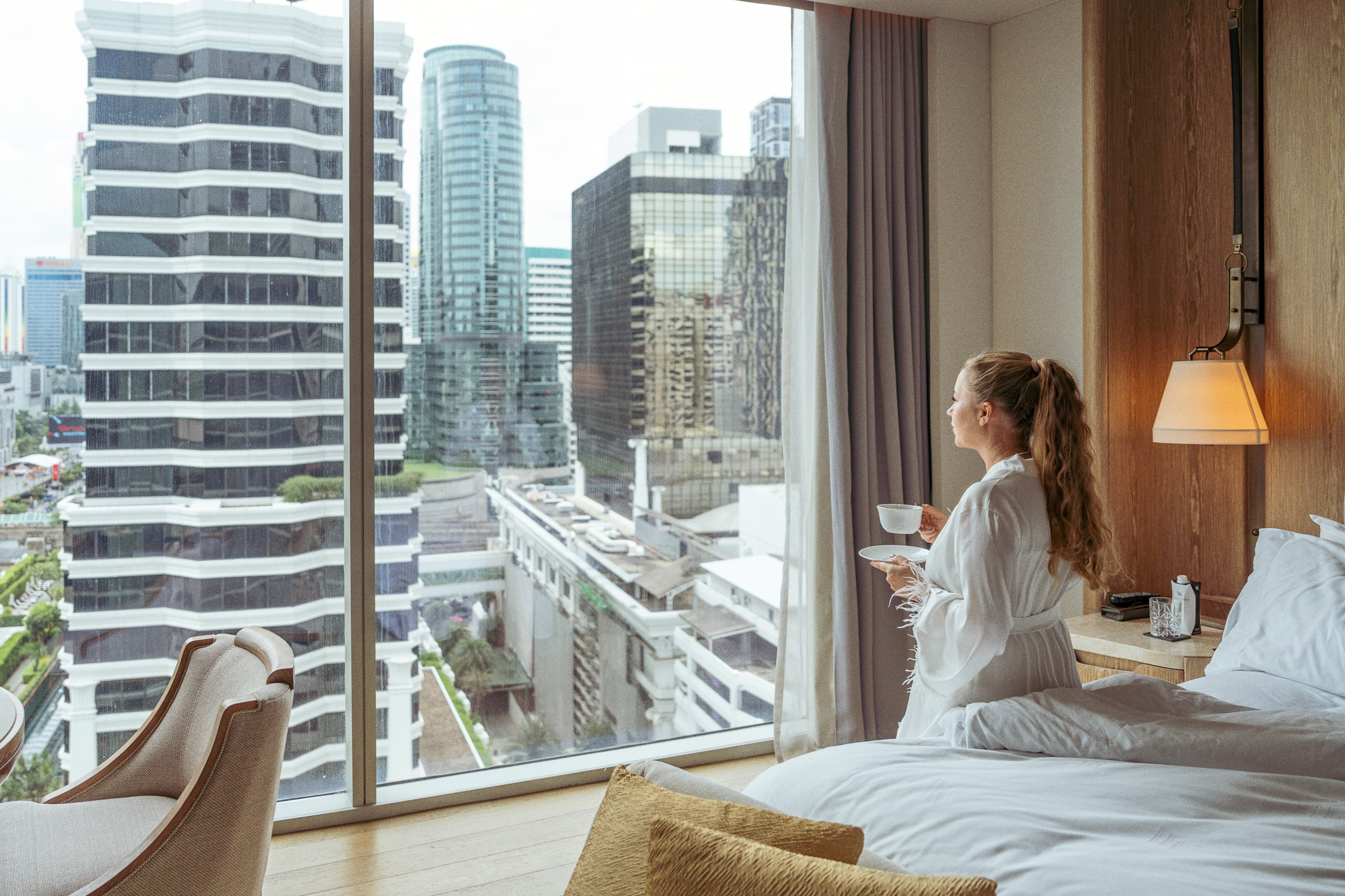 Lifestyle hotel photography at Waldorf Astoria Bangkok featuring a woman enjoying tea with a city view