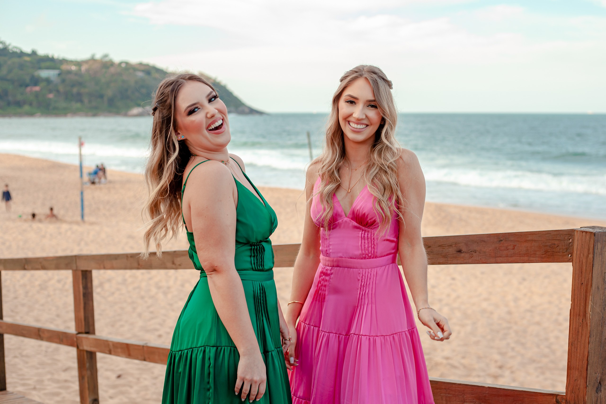 Fotógrafo festa de formatura em Balneário Camboriú; retrato alegre e espontâneo das duas formandas a sorrir juntas na passarela com vista para a praia no Bali Bistro Beach.