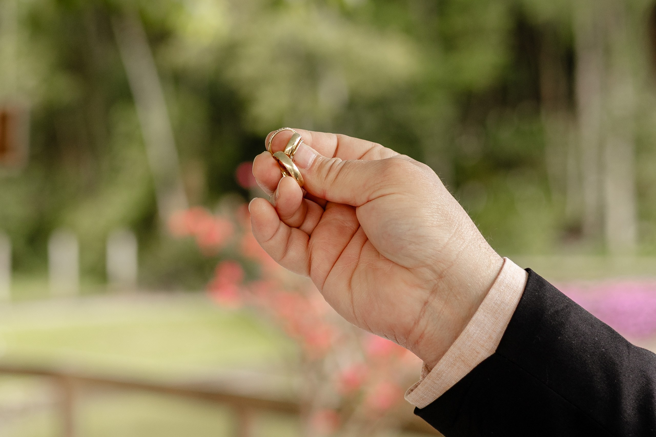 Fotógrafo de casamento em Santa Catarina; mão segurando as alianças de casamento em close com fundo desfocado em área externa.
