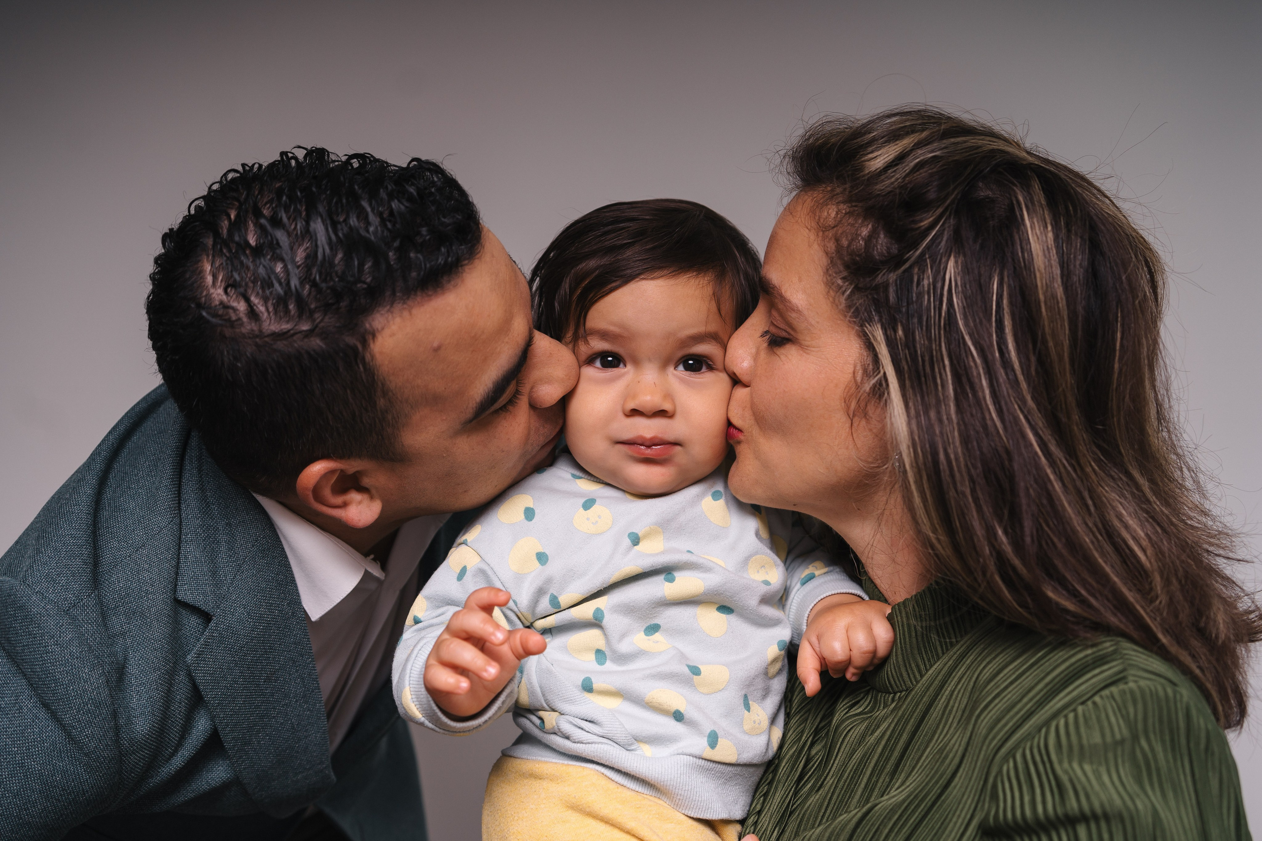 mother and father kissing their baby from both sides in cheeks in Burnaby photo studio