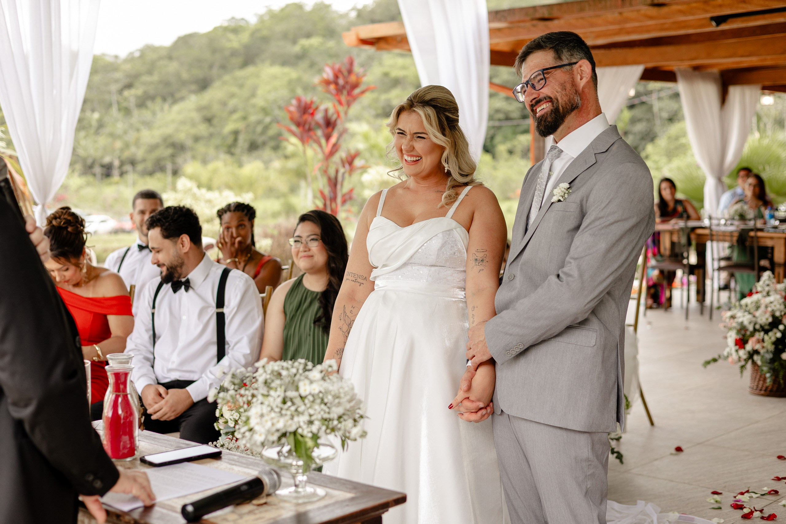 Fotógrafo de casamento em Santa Catarina; noivos sorridentes de mãos dadas no altar durante a cerimônia ao ar livre no campo.