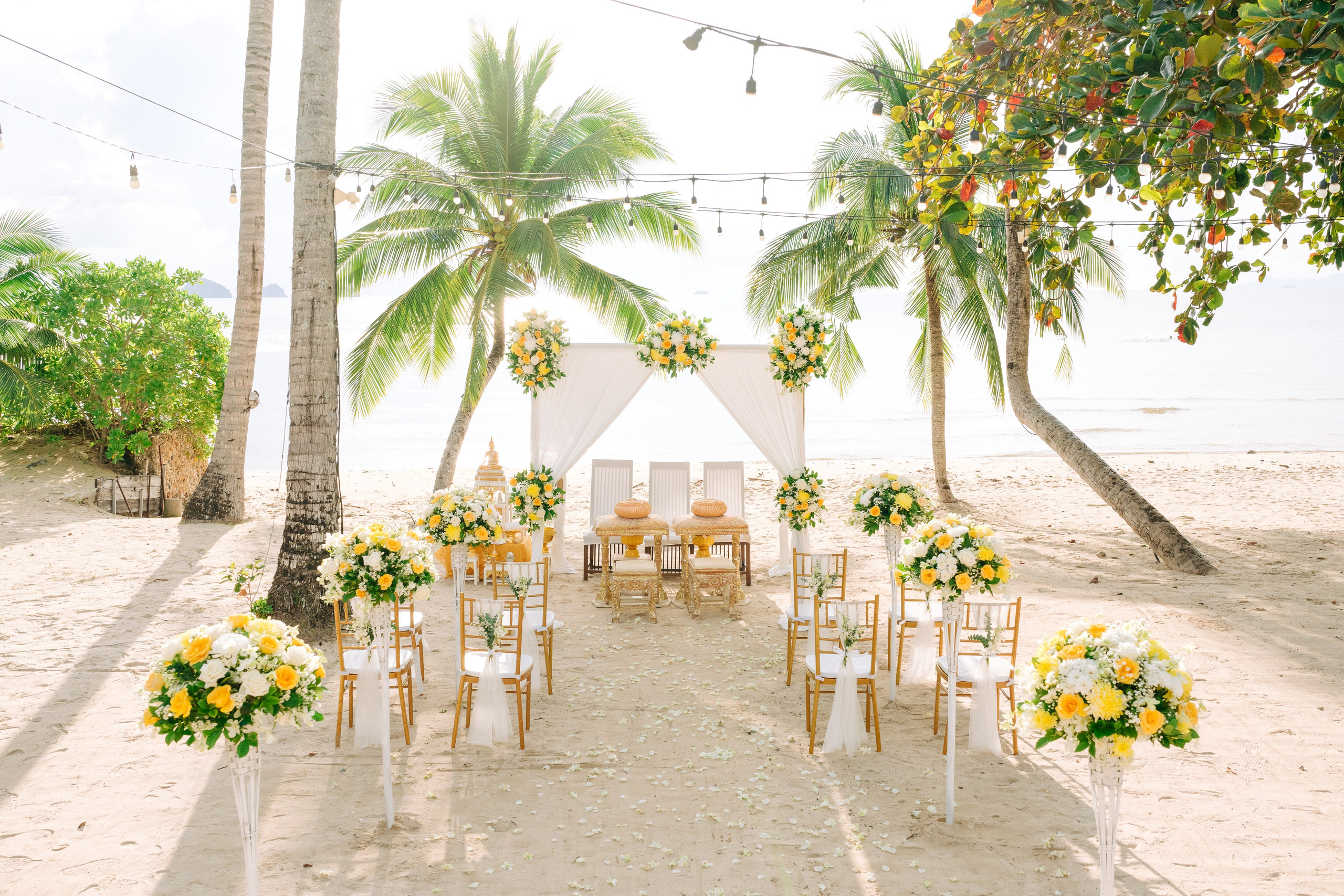 Couple taking part in a traditional Buddhist wedding ceremony on a tropical beach in Koh Samui, Thailand, with monks, flowers, and ocean views.