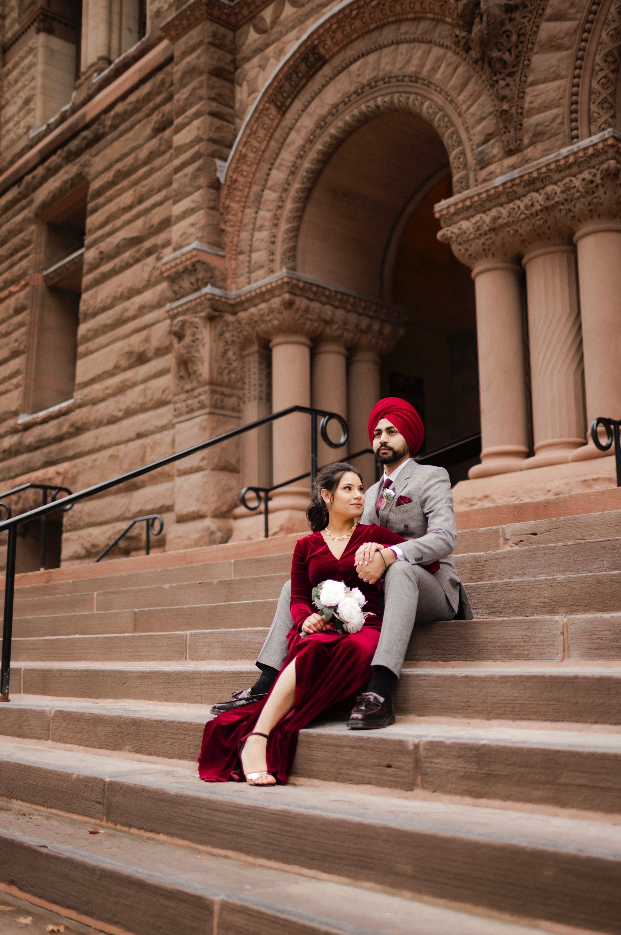 Bride posing on historic building steps in maroon bridal lehenga