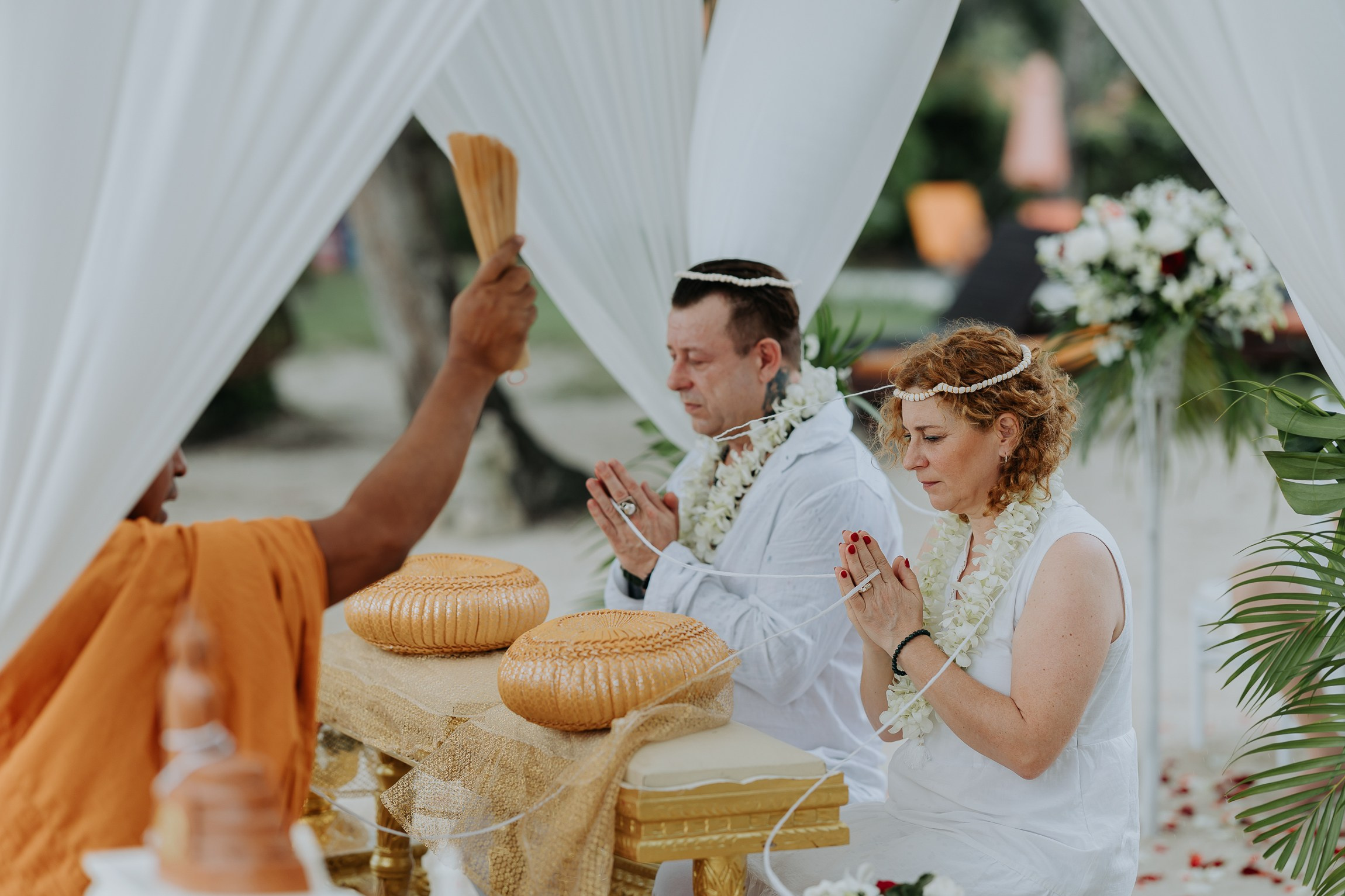 Bride and groom participating in a sacred Buddhist wedding blessing in Thailand