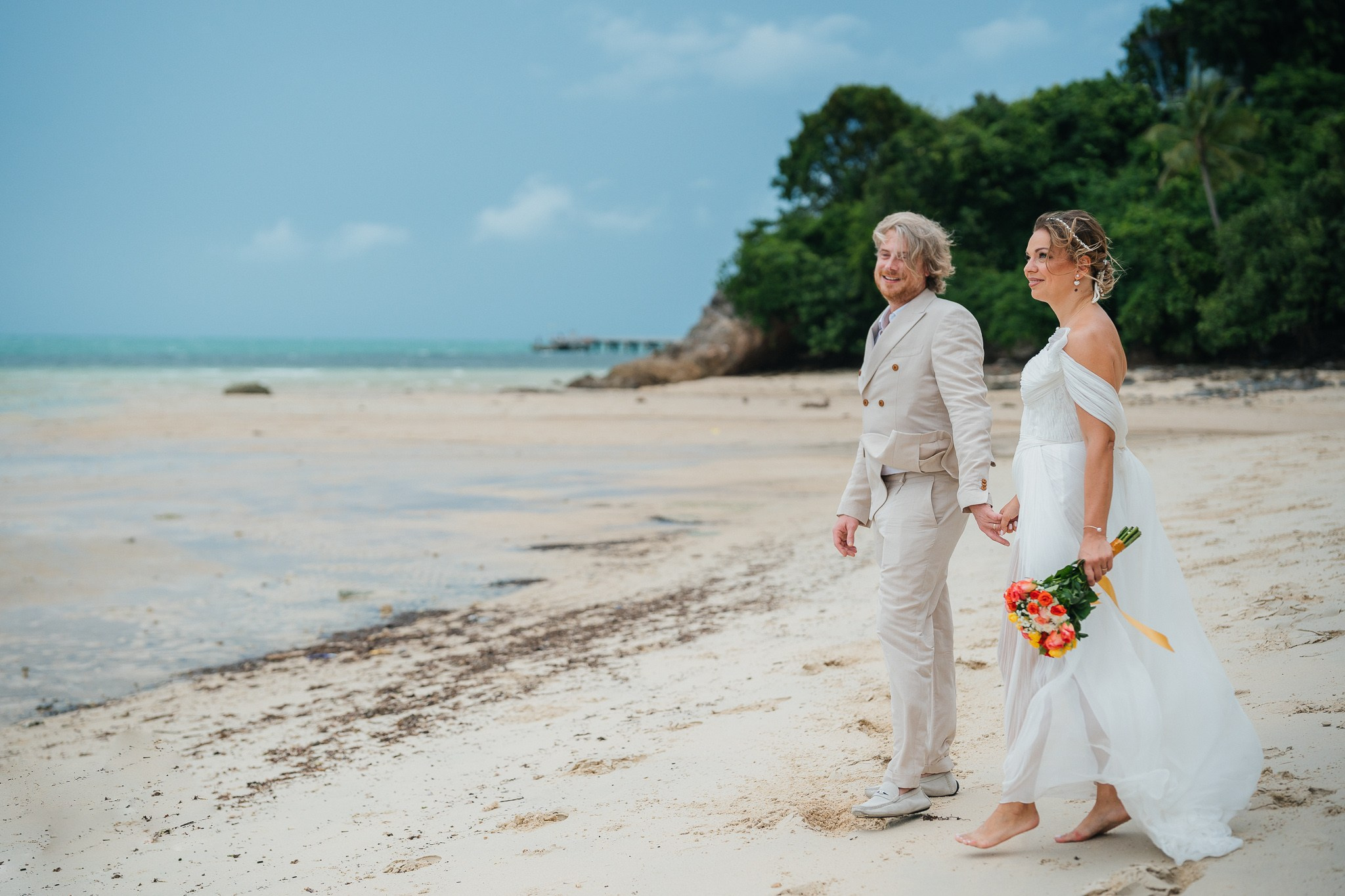 Couple taking part in a traditional Buddhist wedding ceremony on a tropical beach in Koh Samui, Thailand, with monks, flowers, and ocean views.
